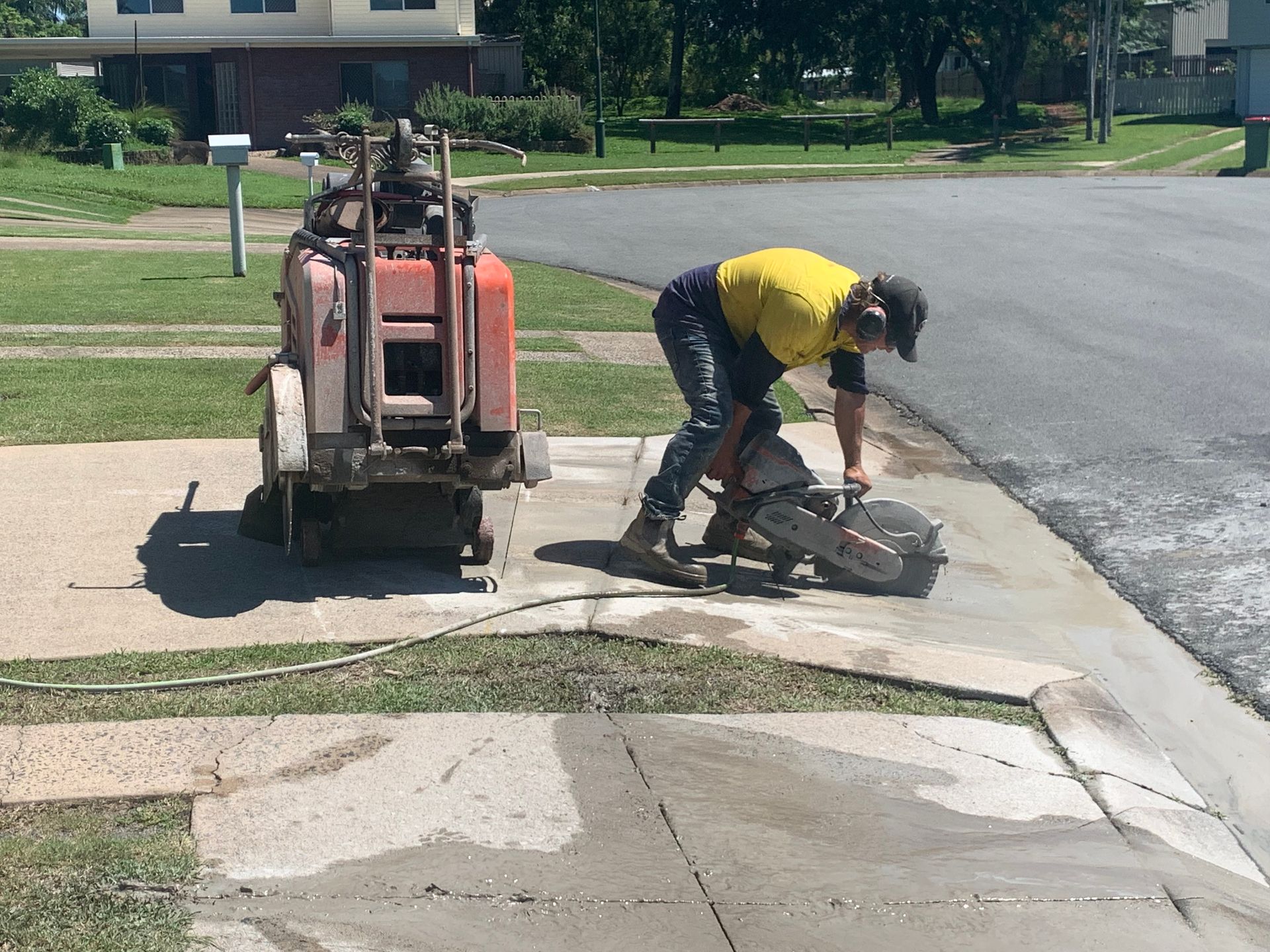 Man in Yellow Shirt Cuts Concrete Sidewalk With a Saw — Ablecut Concrete Cutting & Coring In East Mackay, QLD