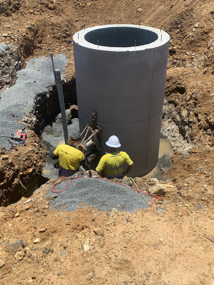 Two workers in yellow shirts installing a large concrete cylinder in a construction site— Ablecut Concrete Cutting & Coring In Marian, QLD