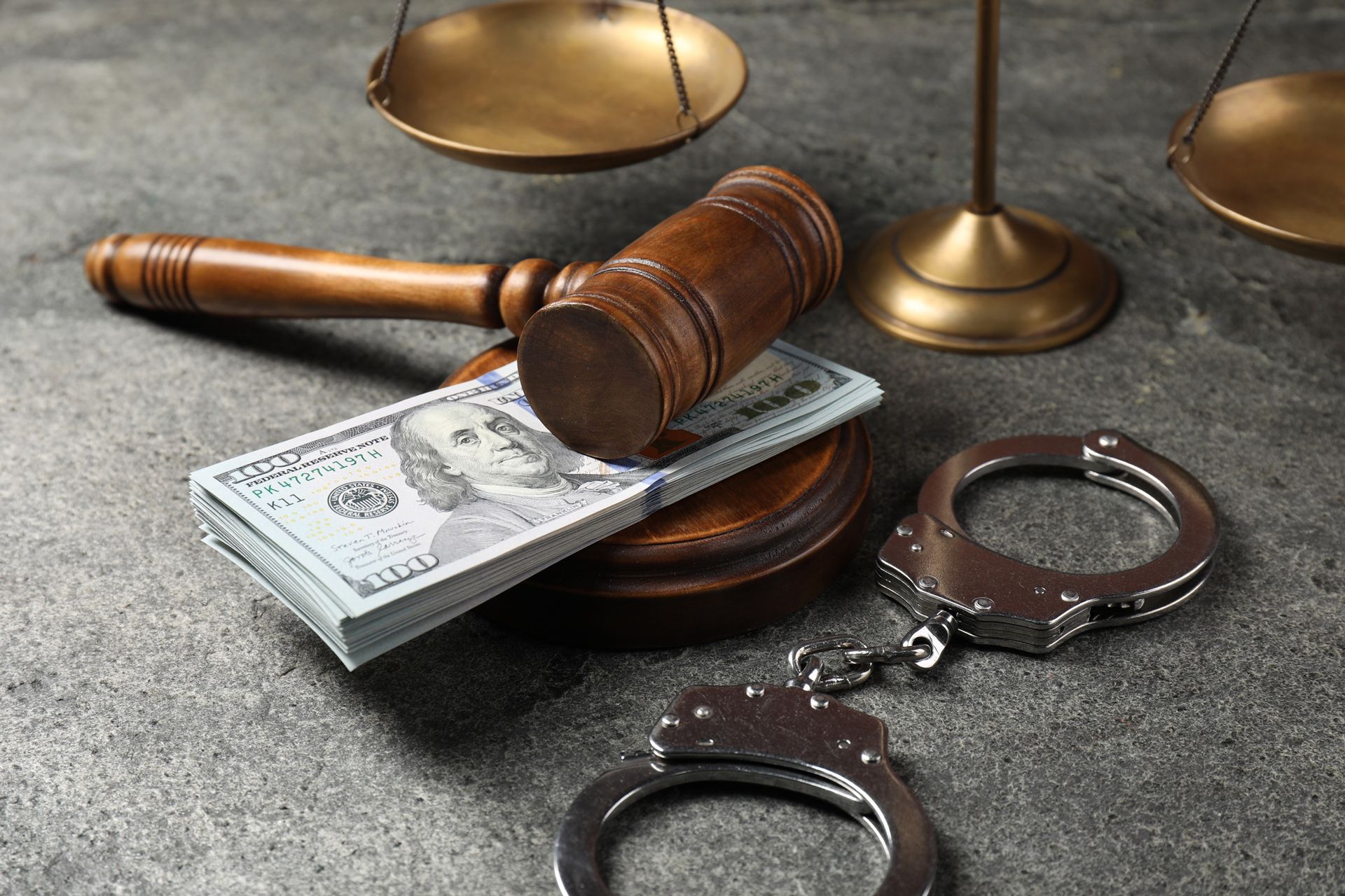 Gavel, scales of justice, stack of money, and handcuffs on a gray surface, representing justice and legal proceedings. Gavel, scales of justice, stack of money, and handcuffs on a gray surface, representing justice and legal proceedings.