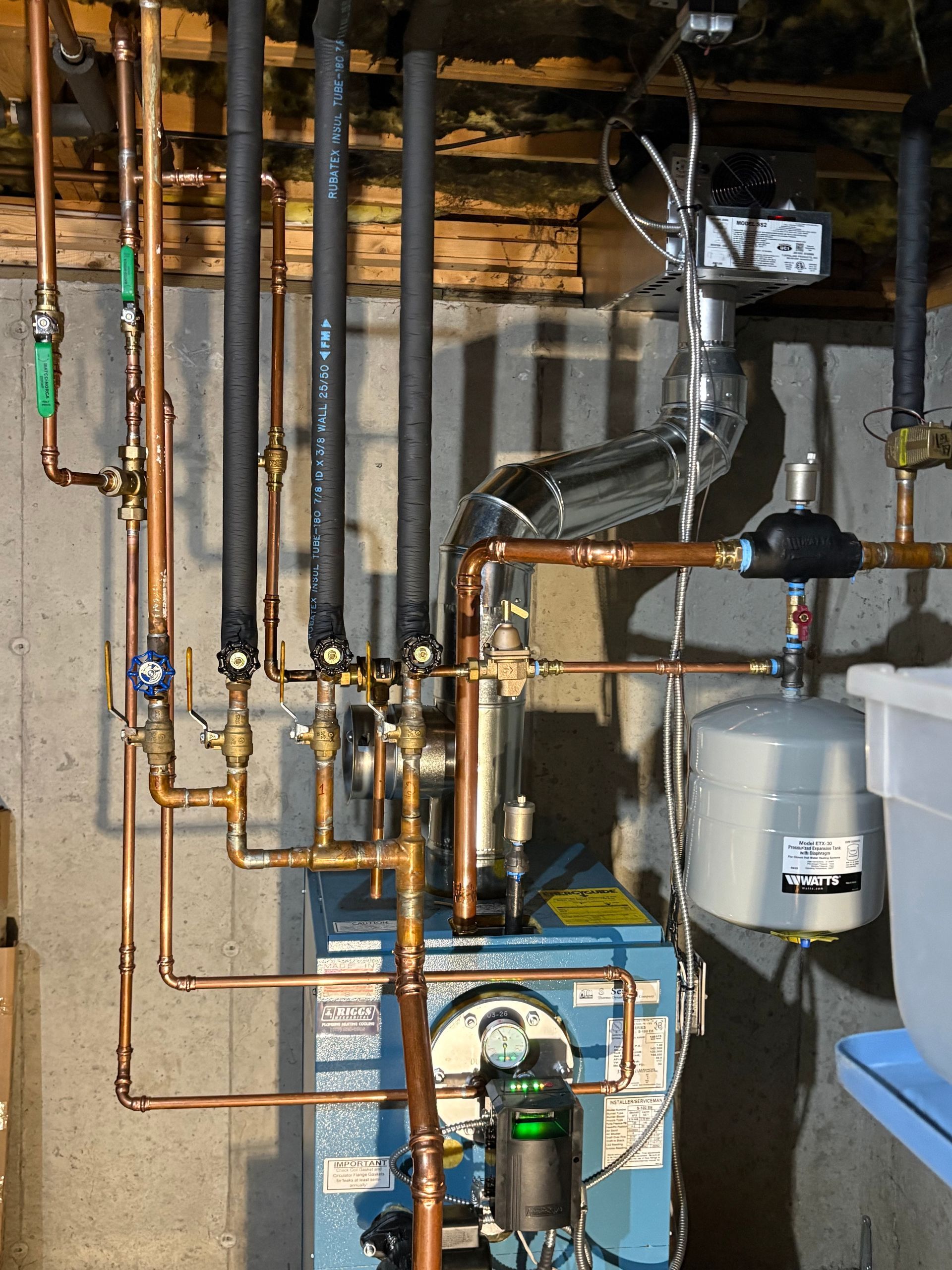 Copper pipes and water heater on a wooden wall. Various gauges, valves, and electrical components present.