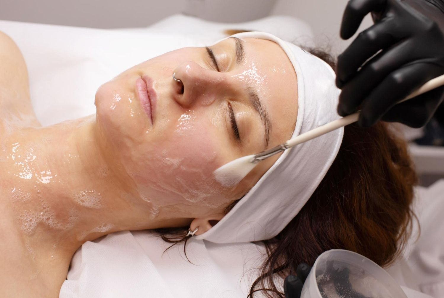 Woman receiving a facial treatment with cream applied to her face and a brush near her cheek