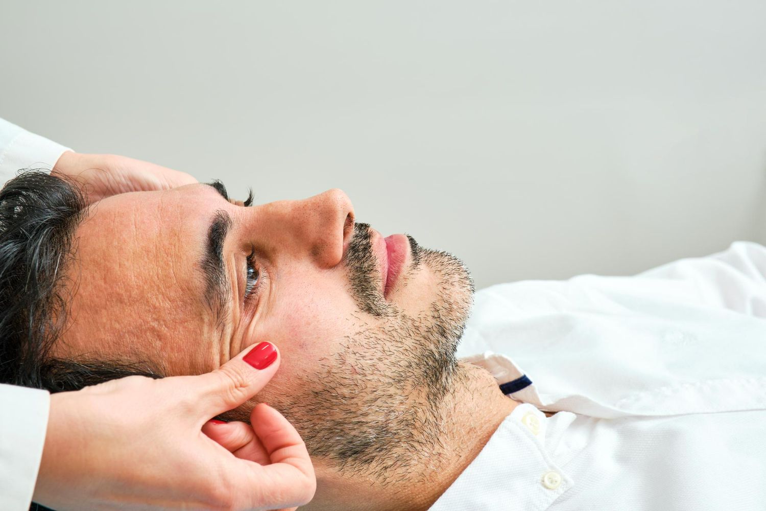 Man lying down while a hand applies makeup or facial treatment near his cheek