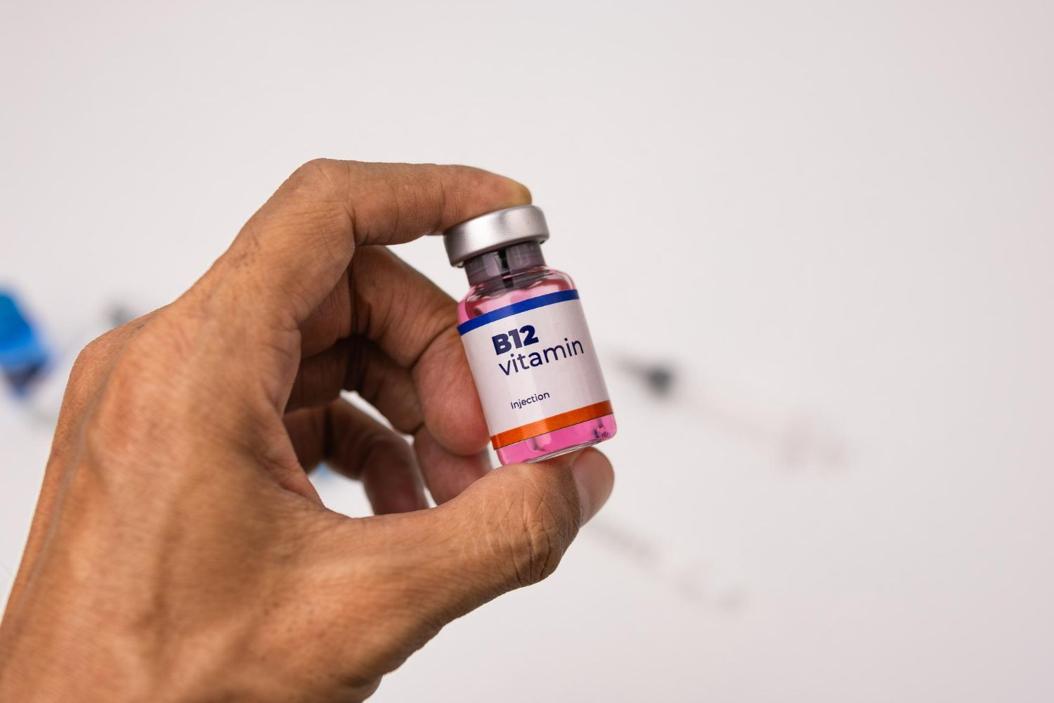 Hand holding a small vitamin B12 vial against a blurred light background