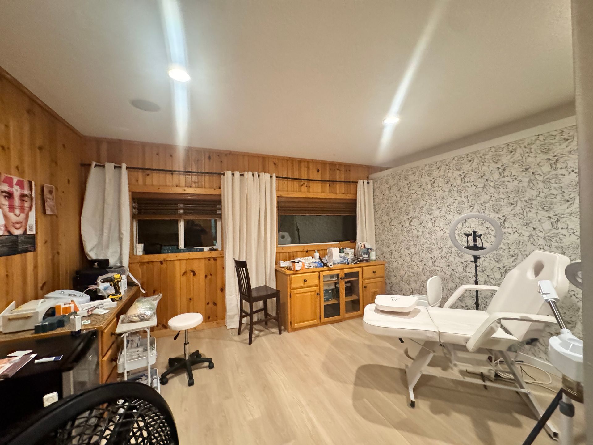 Salon interior with white bed, ring light, wooden walls, and work station.