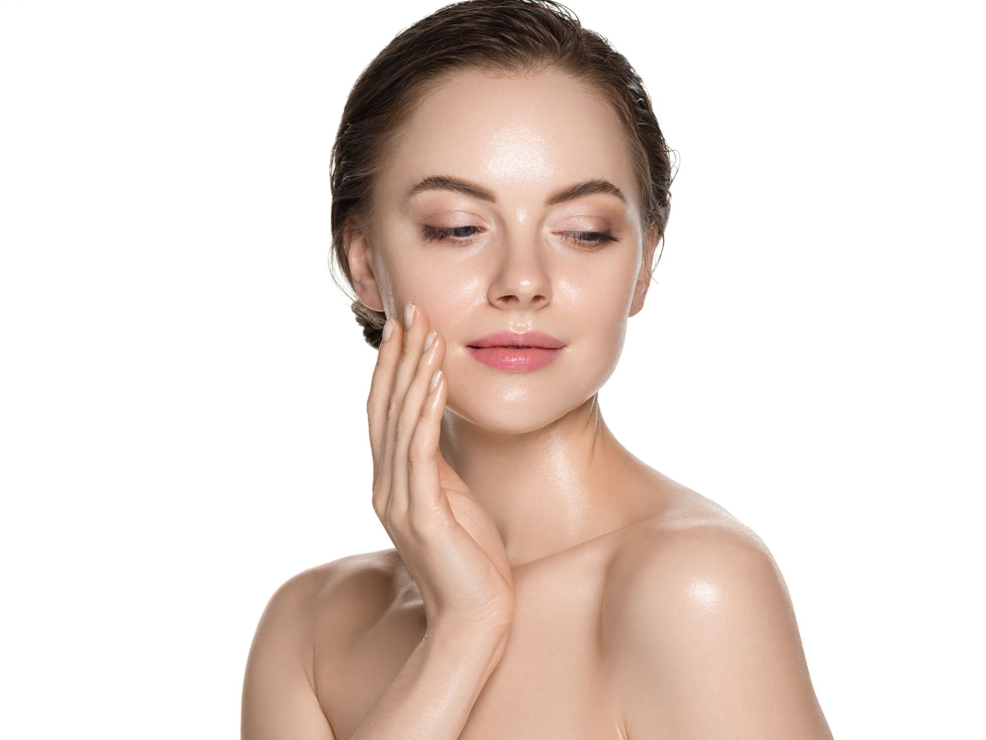 Woman with glowing skin, touching her face, looking down, white background.