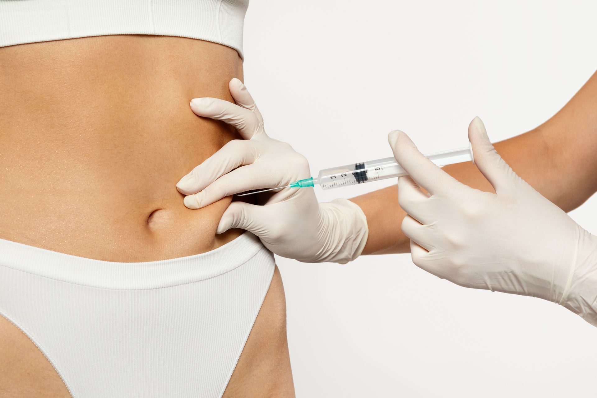 Hands in gloves administering an injection into a person's abdomen.