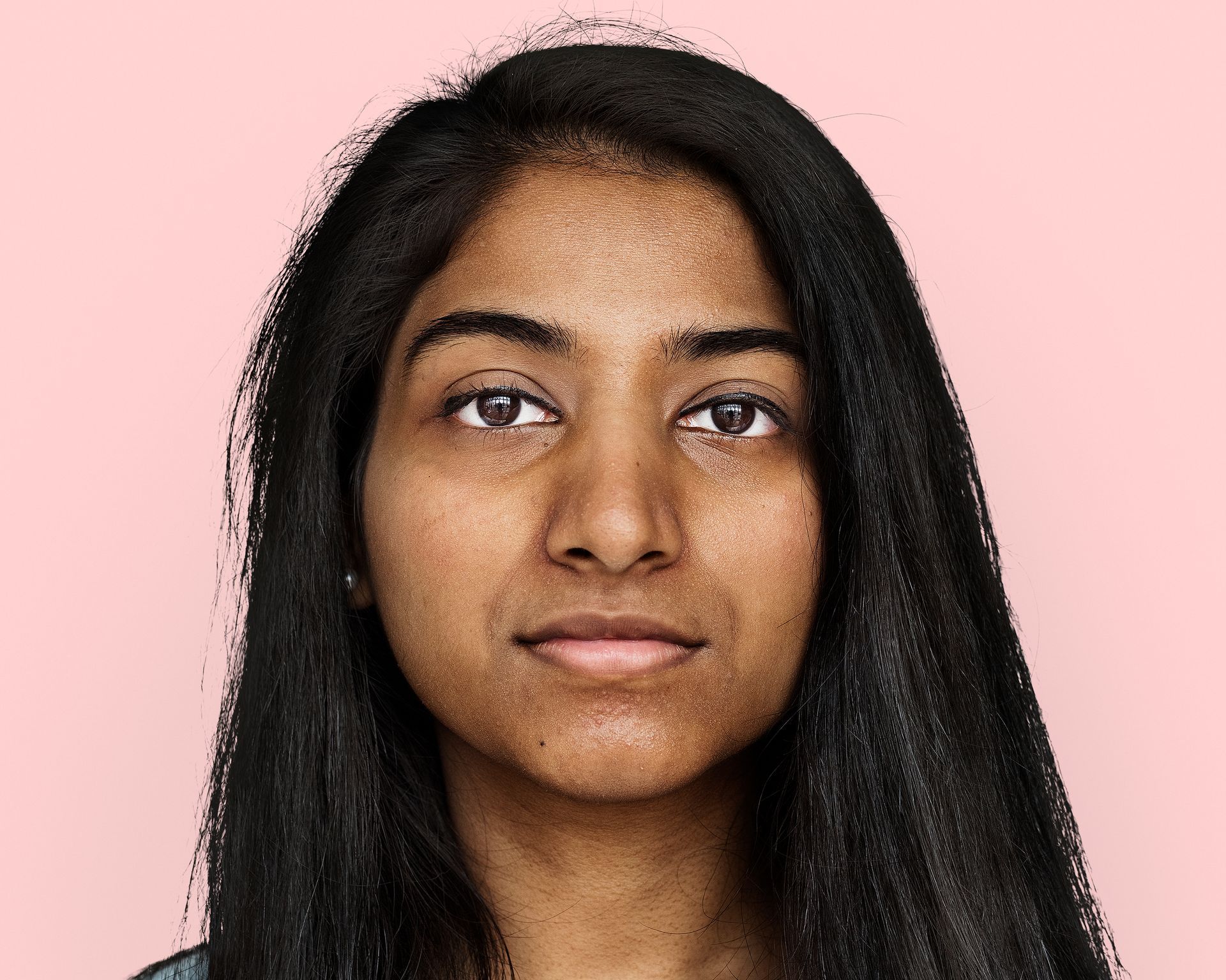 Woman with long dark hair, looking directly at the viewer, against a pink background.