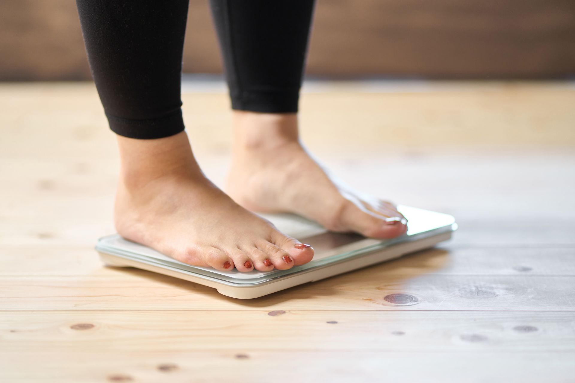 Feet standing on a bathroom scale on a wooden floor.