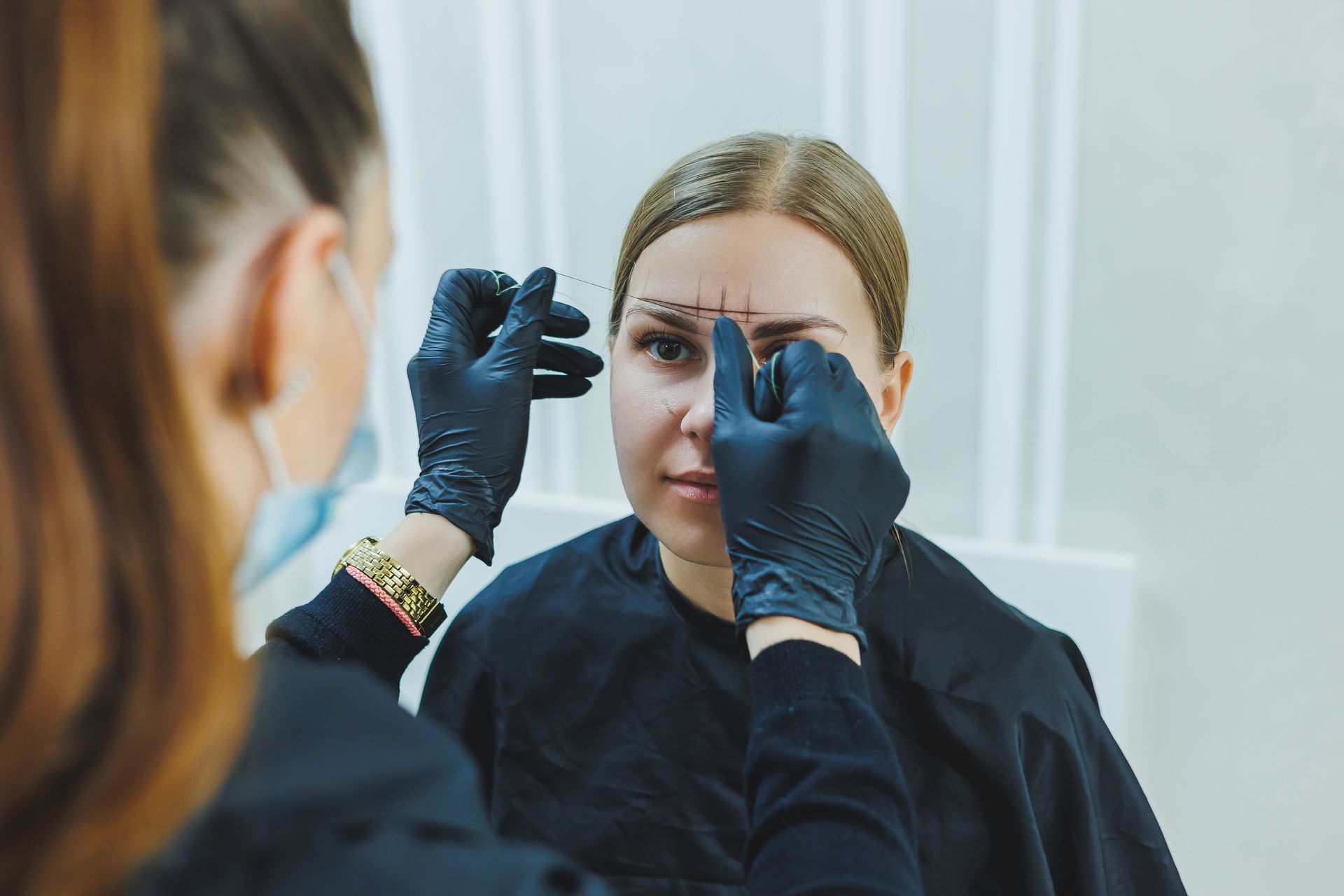 Woman in blue gloves applying makeup to another woman’s face in a salon setting