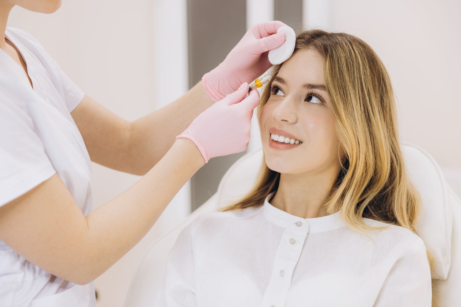 A clinician applying a facial treatment to a smiling patient in a bright clinic.