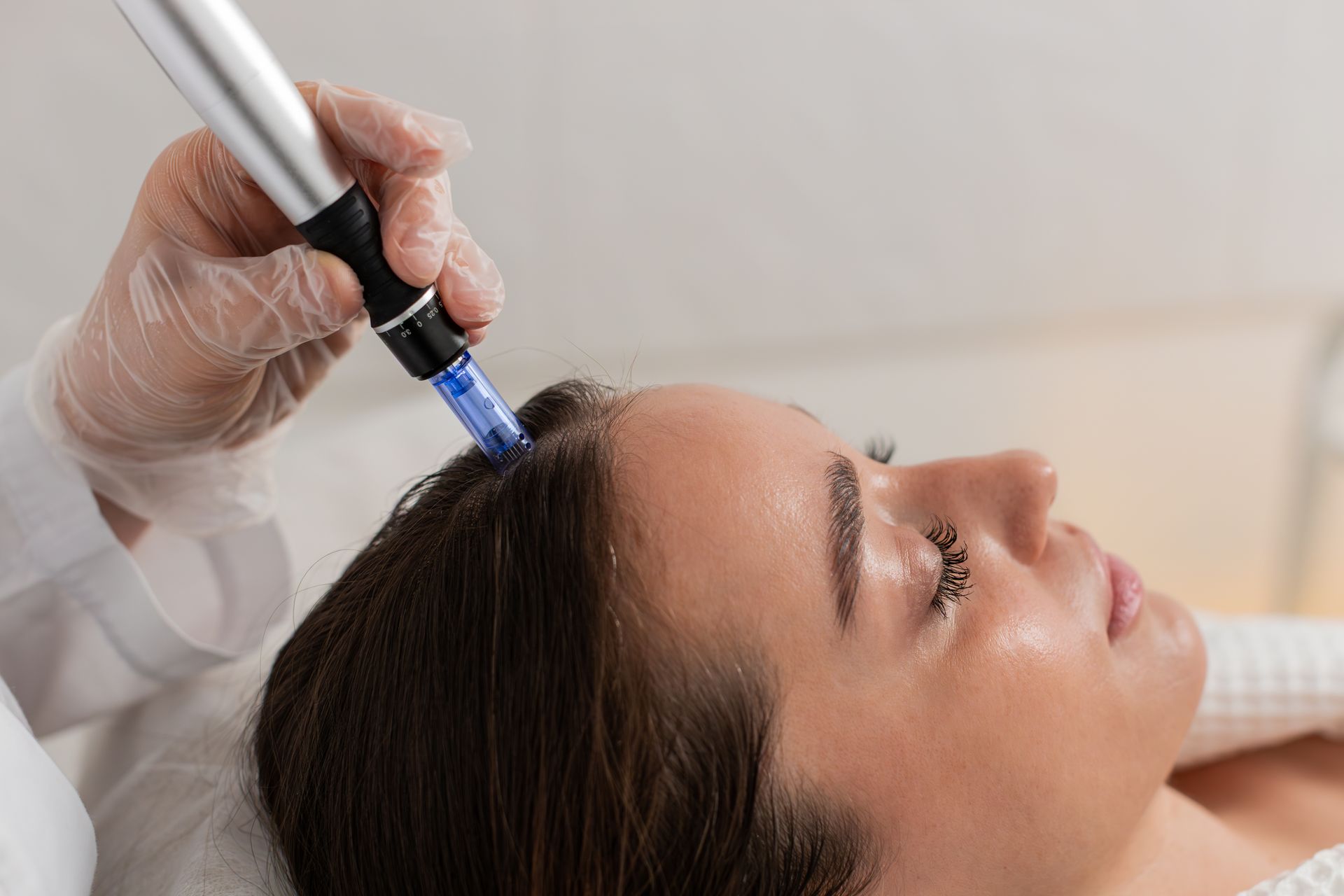 A person receiving a scalp treatment with a microneedling device at a clinic.