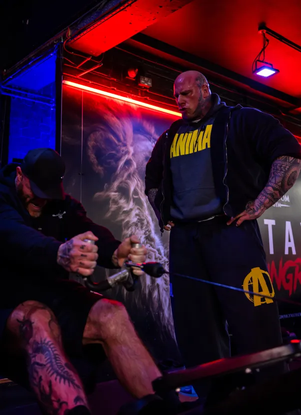 A muscular man in a black shirt and shorts, fist clenched, looks forward.