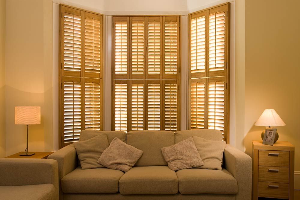 Living room with sofa, lamps, and wood shutters on bay window.