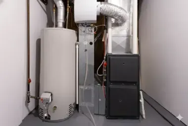 Water heater, furnace, and ventilation in a basement corner with gray and white walls.