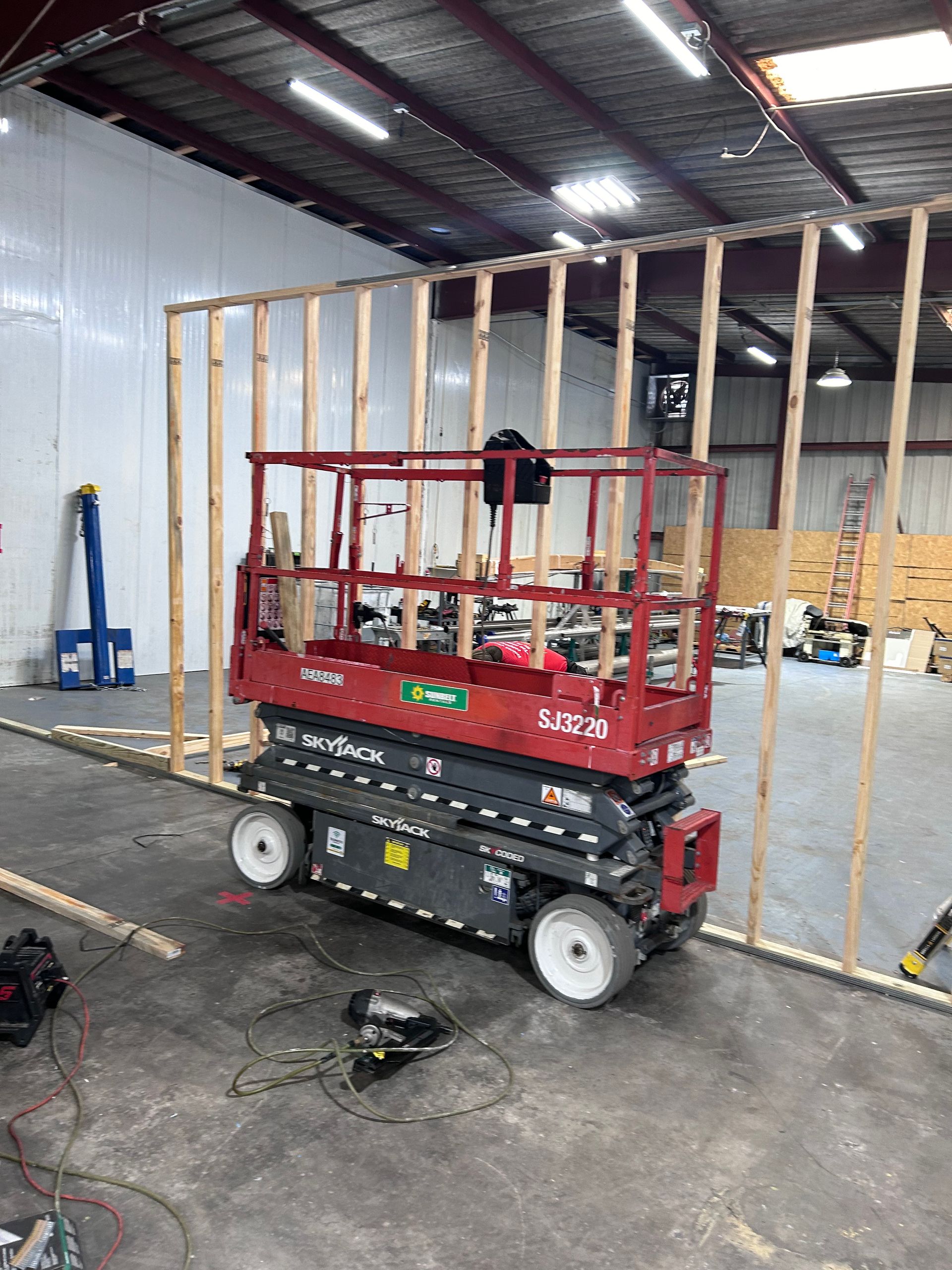 A red scissor lift is sitting in a warehouse under construction.