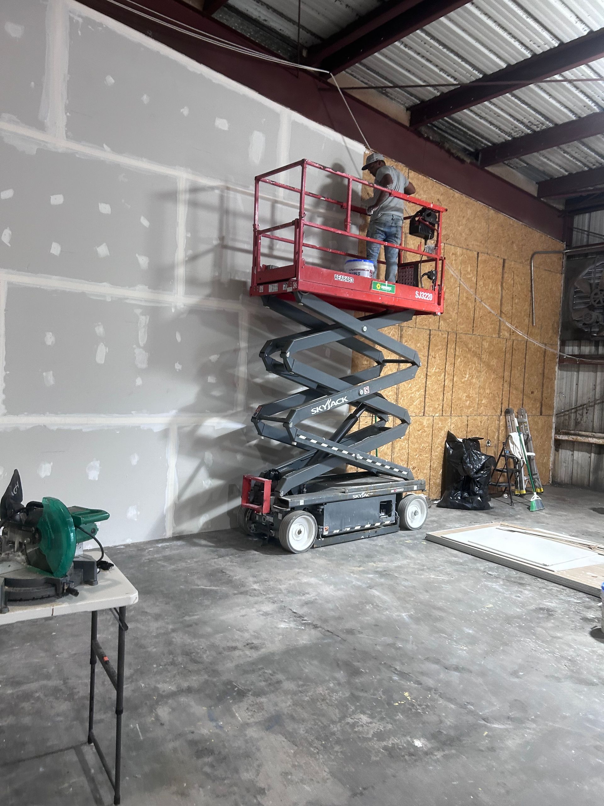 A man is standing on a scissor lift working on a wall.