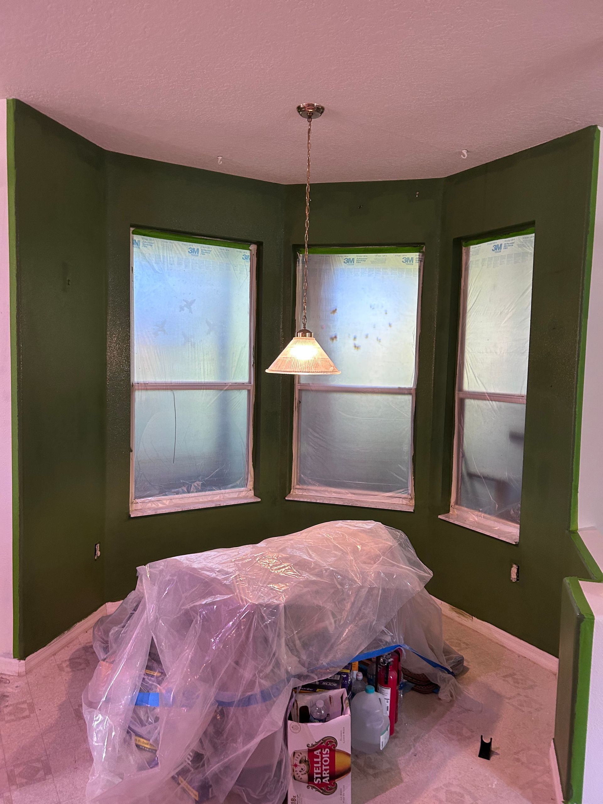 A room with green walls and windows is being painted.