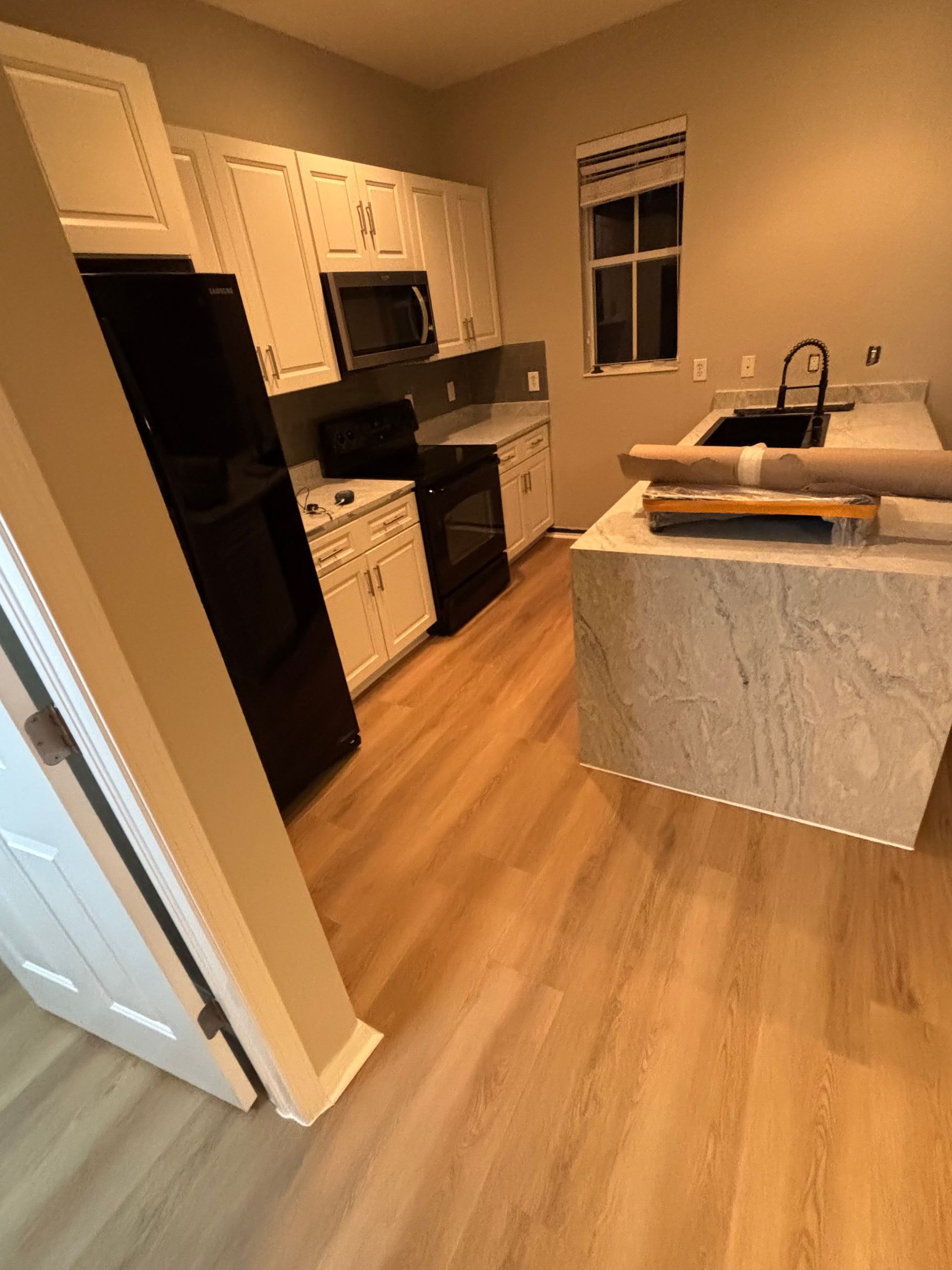 Kitchen with white cabinets, black appliances, light wood flooring, and a gray countertop.