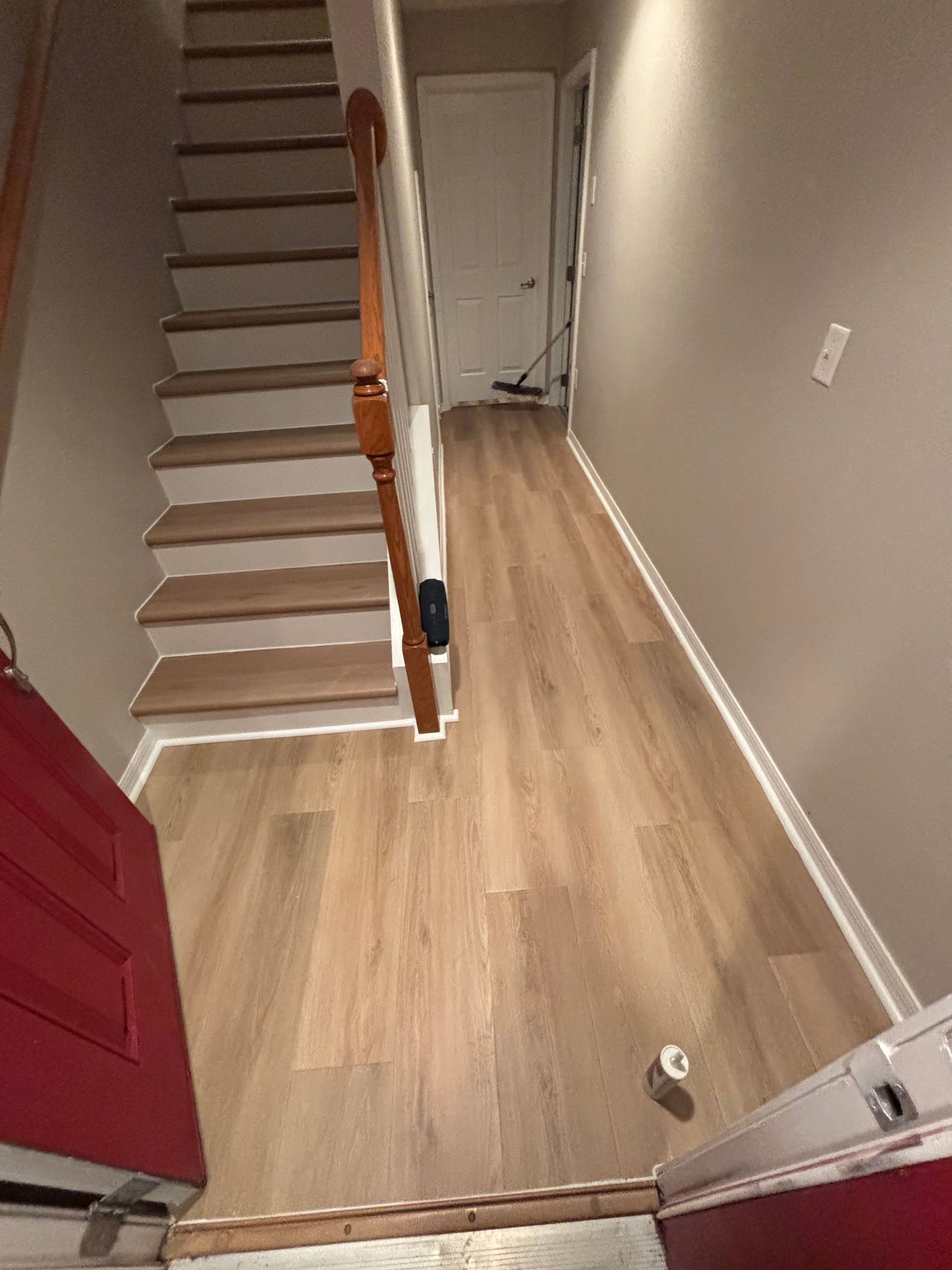 Stairway with wood-look flooring and a white door at the end of the hallway. Red door on the left.
