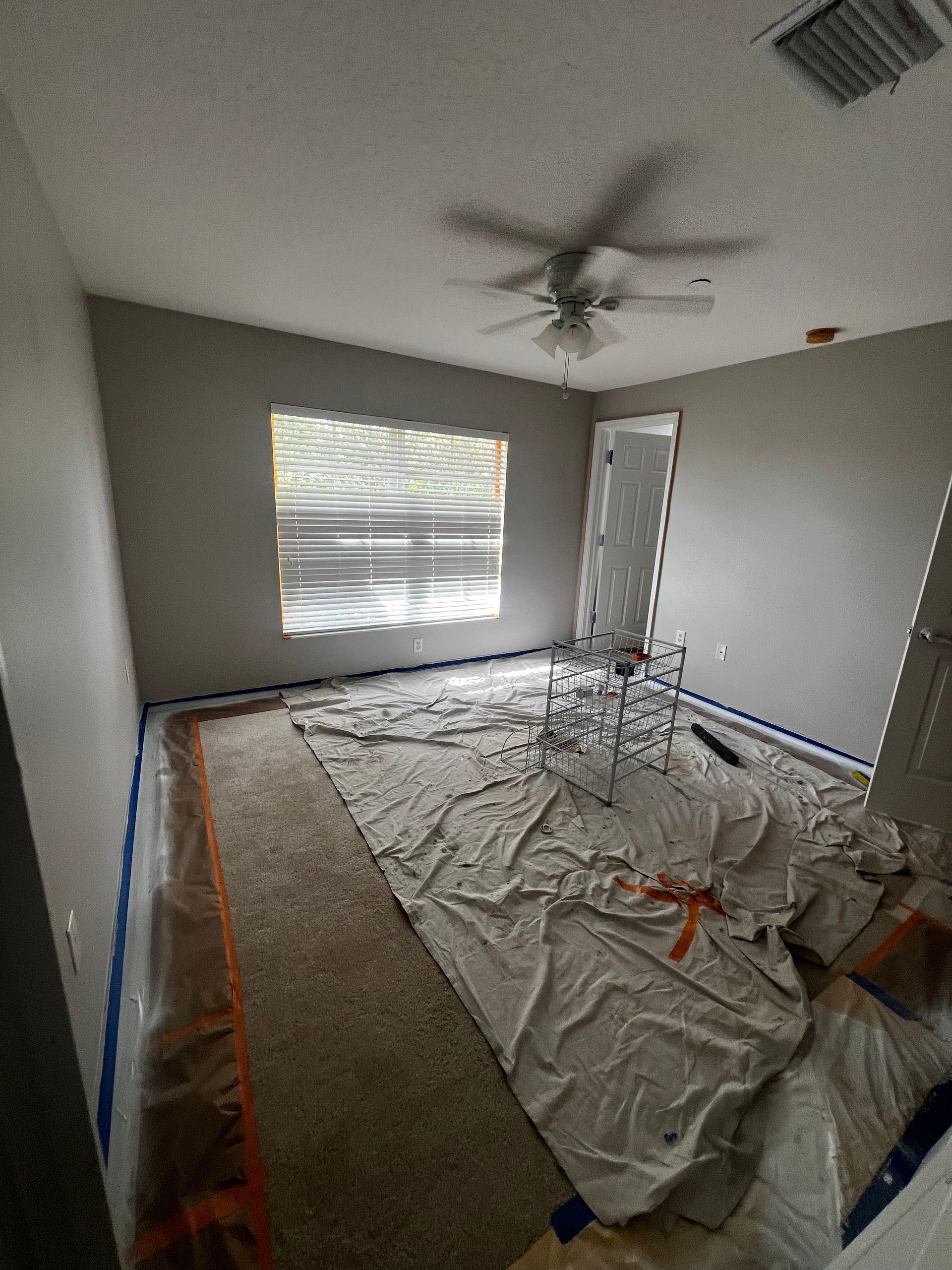 Room with tan carpet, painted walls, covered furniture, and a window.