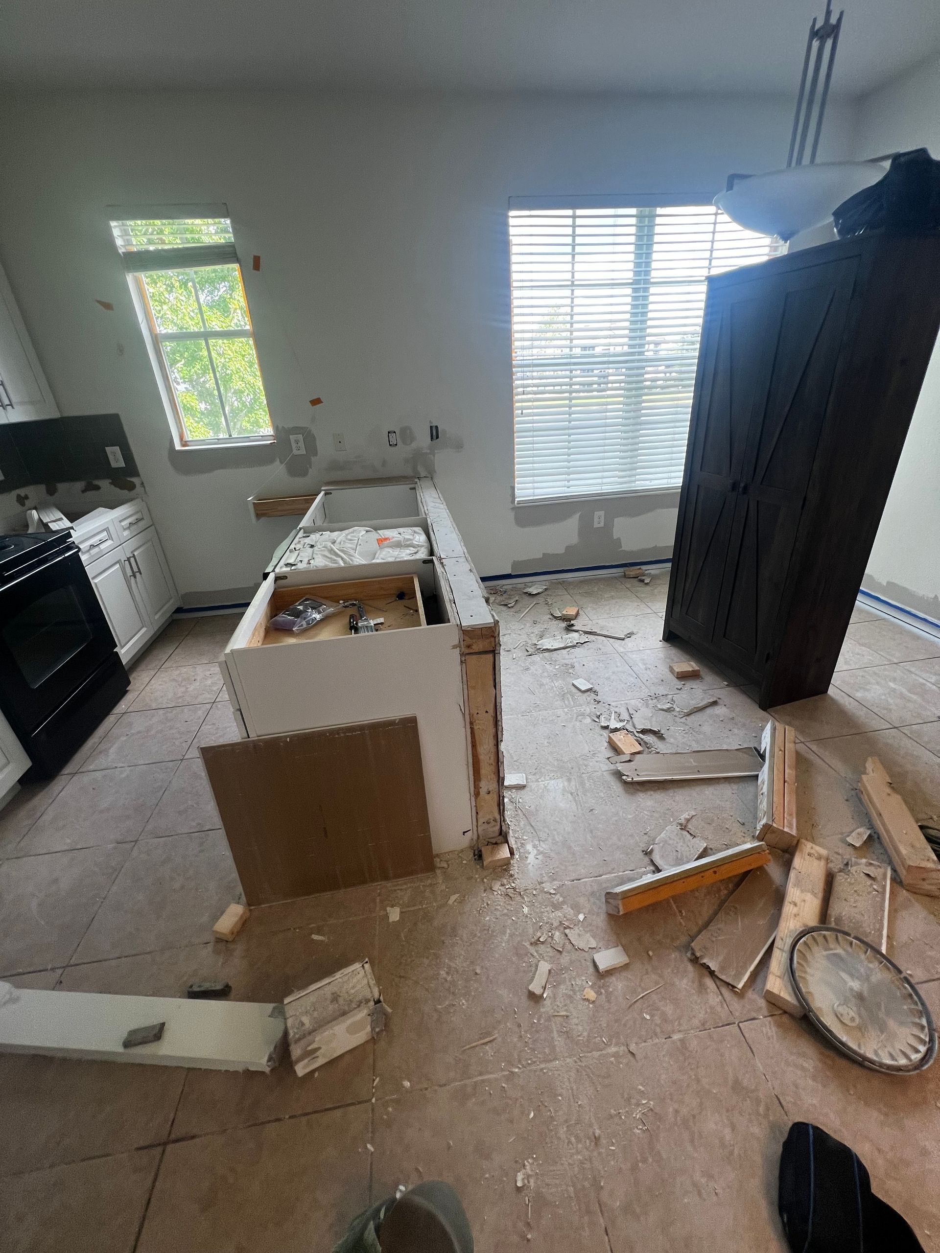 Kitchen under renovation; debris on floor, white cabinets, island partially demolished, window.