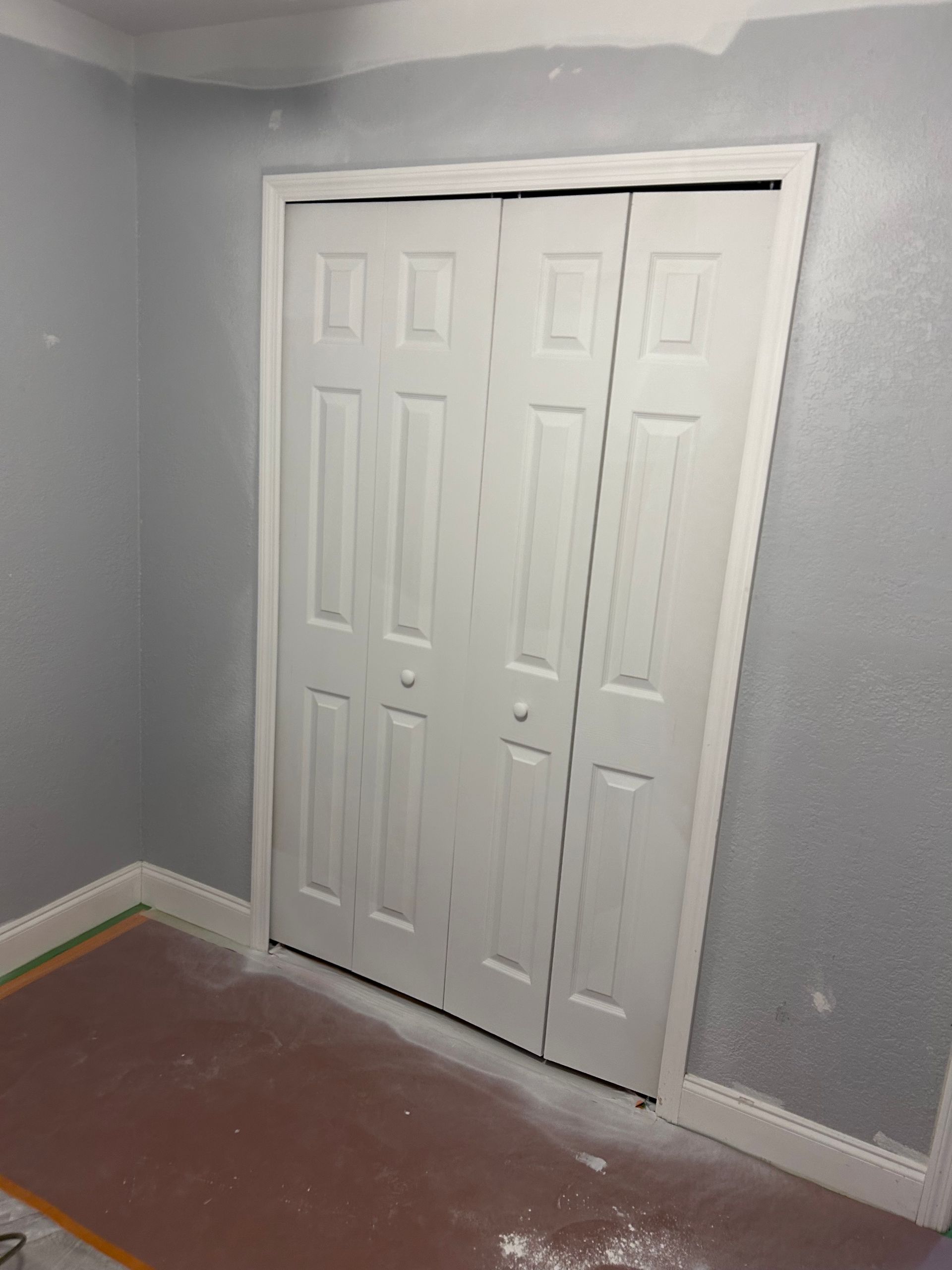 White bi-fold closet doors in a room with gray walls and a red floor.
