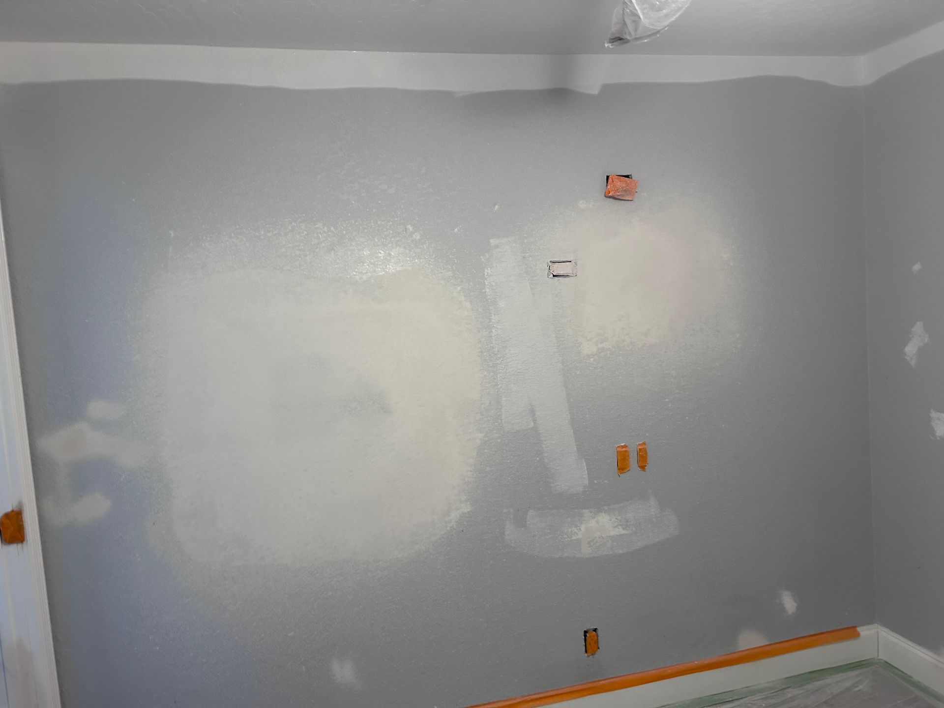 Gray painted interior wall with light patches, electrical fixtures, and wood trim.