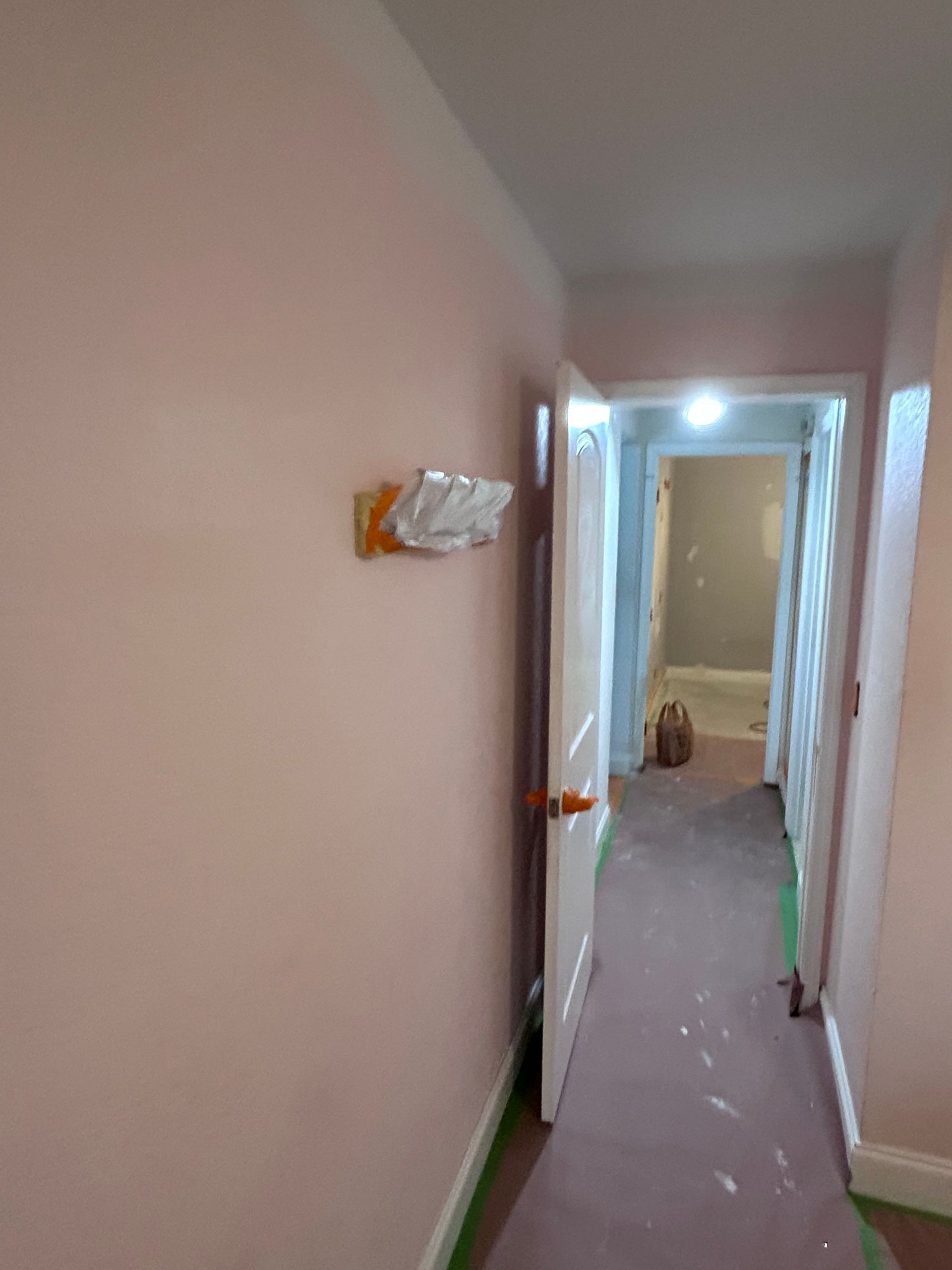 A hallway with light pink walls, a partially open white door, and a light fixture on the left.