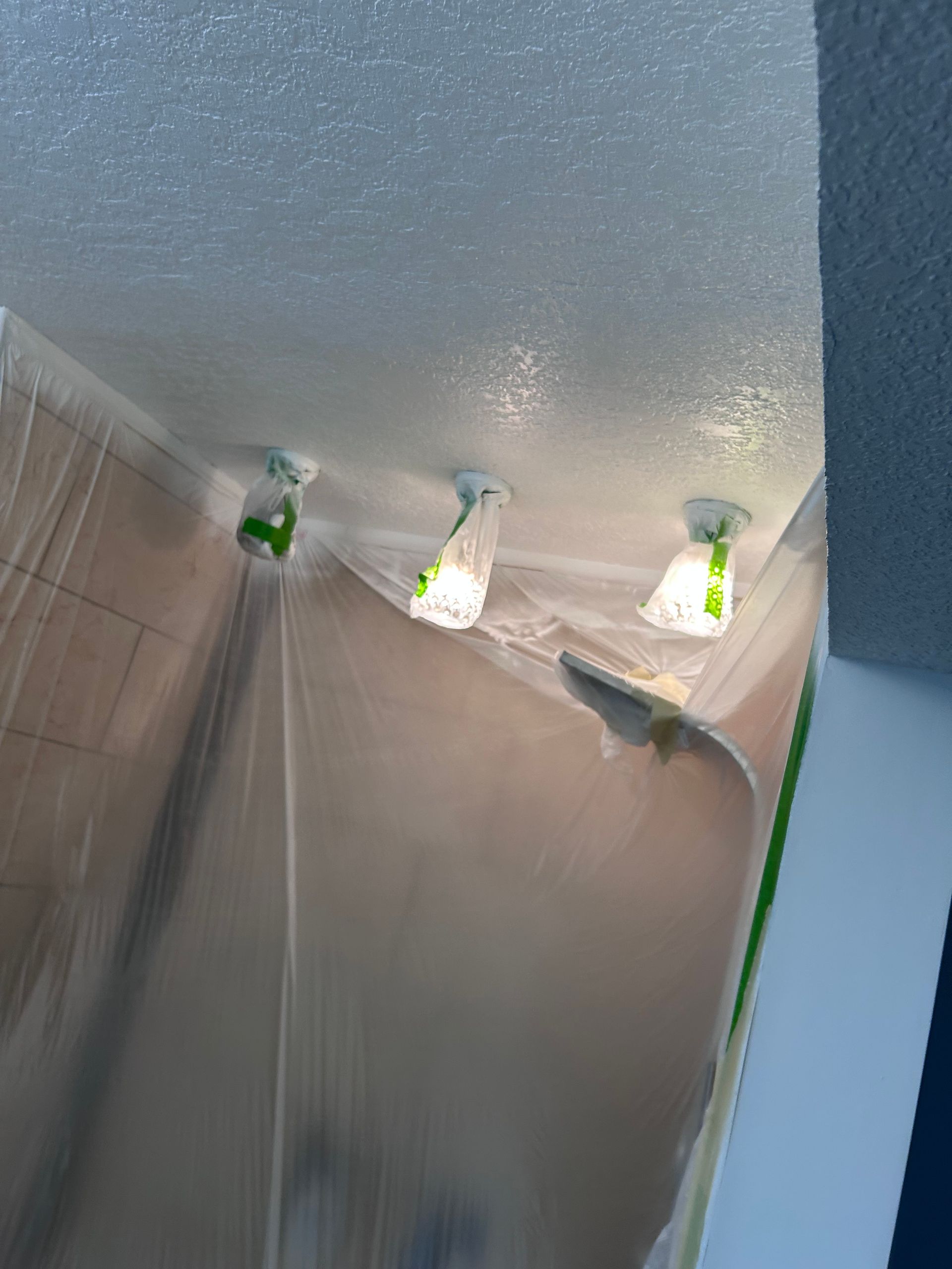 Three ceiling lights covered in plastic, likely for painting, in a room.
