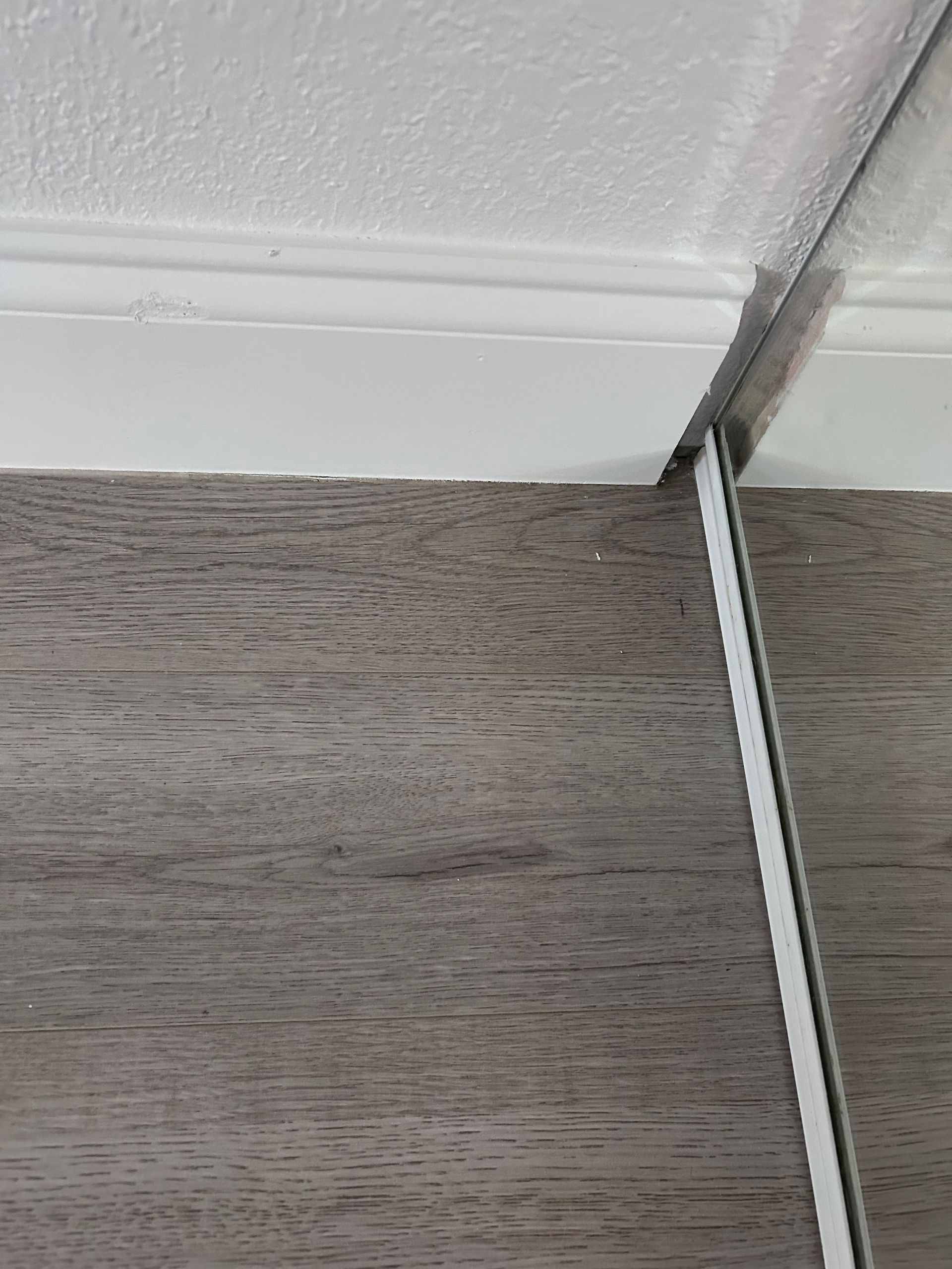 Close-up of a wall with wood paneling, white molding, and a mirror with a silver frame.