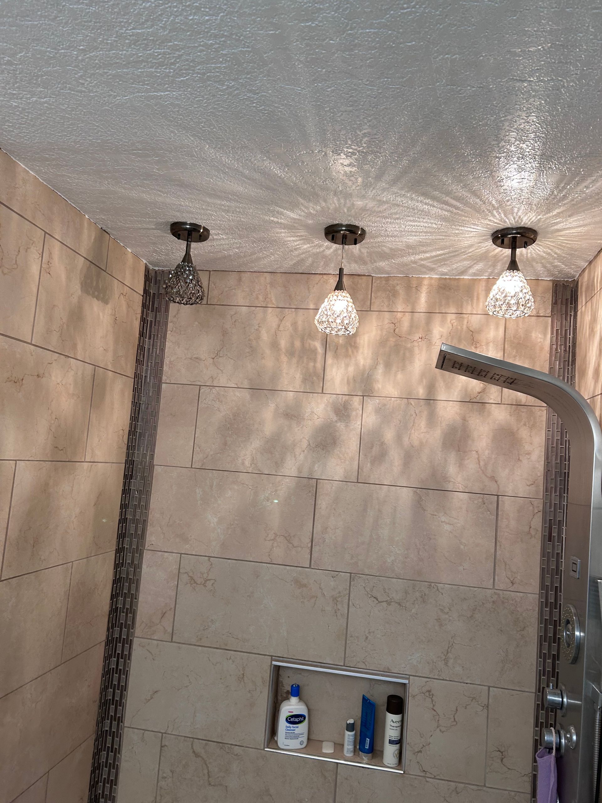 Shower with beige tiles, pebble accents, and three pendant lights casting starburst patterns.