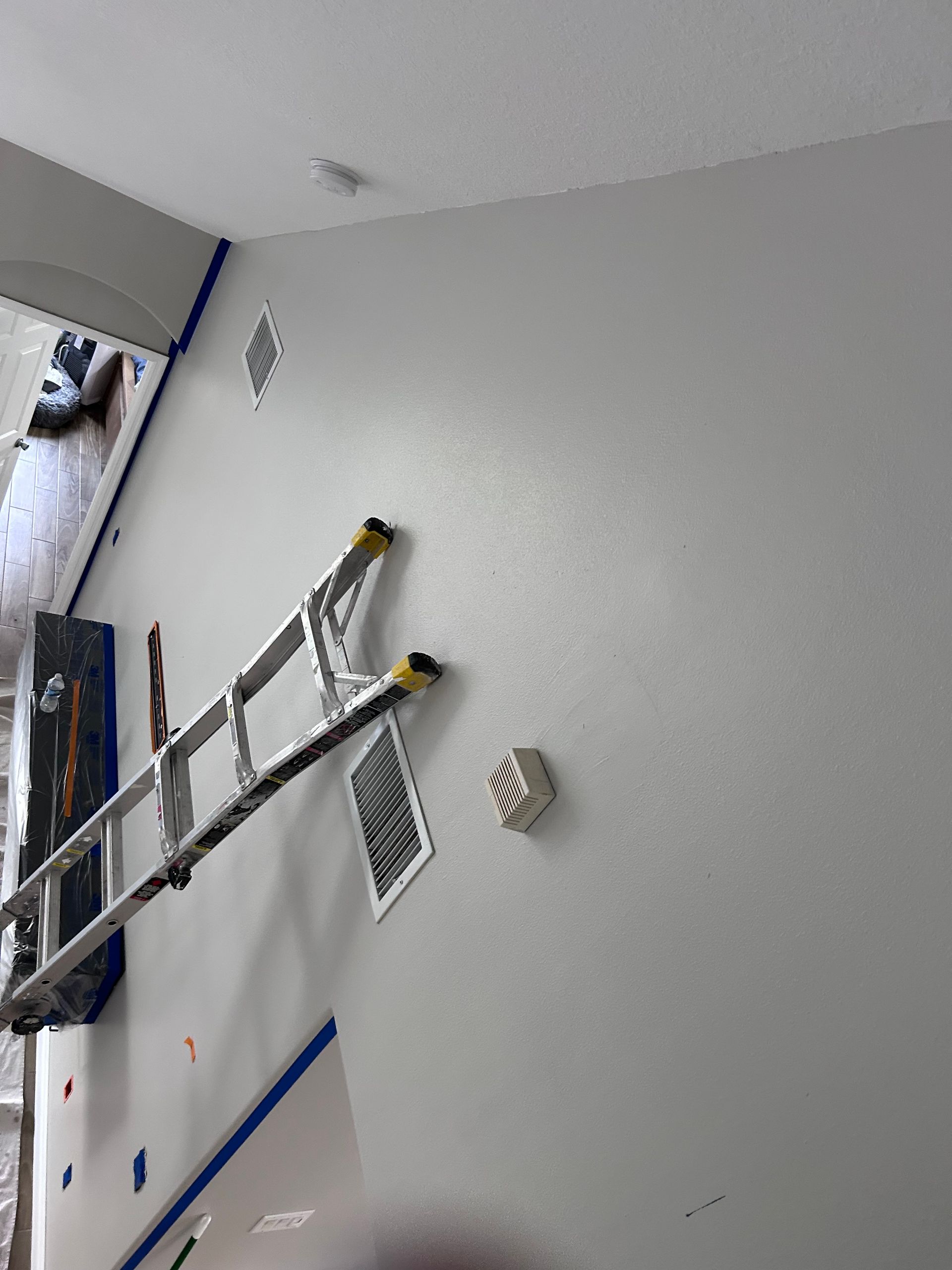 Ladder on a freshly painted gray wall, masking tape visible, near vents.