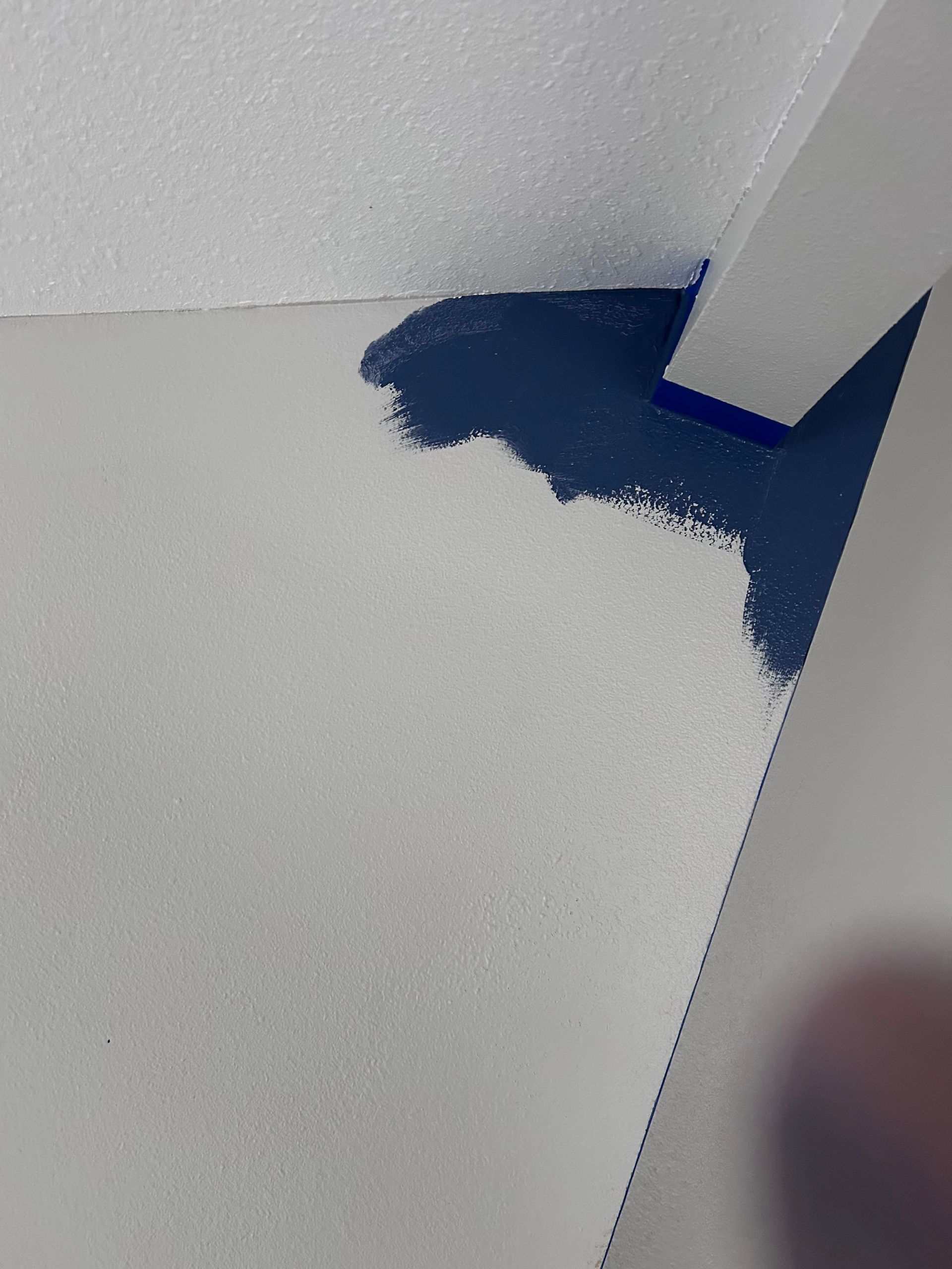 Blue paint being applied to a white surface using a paint scraper.