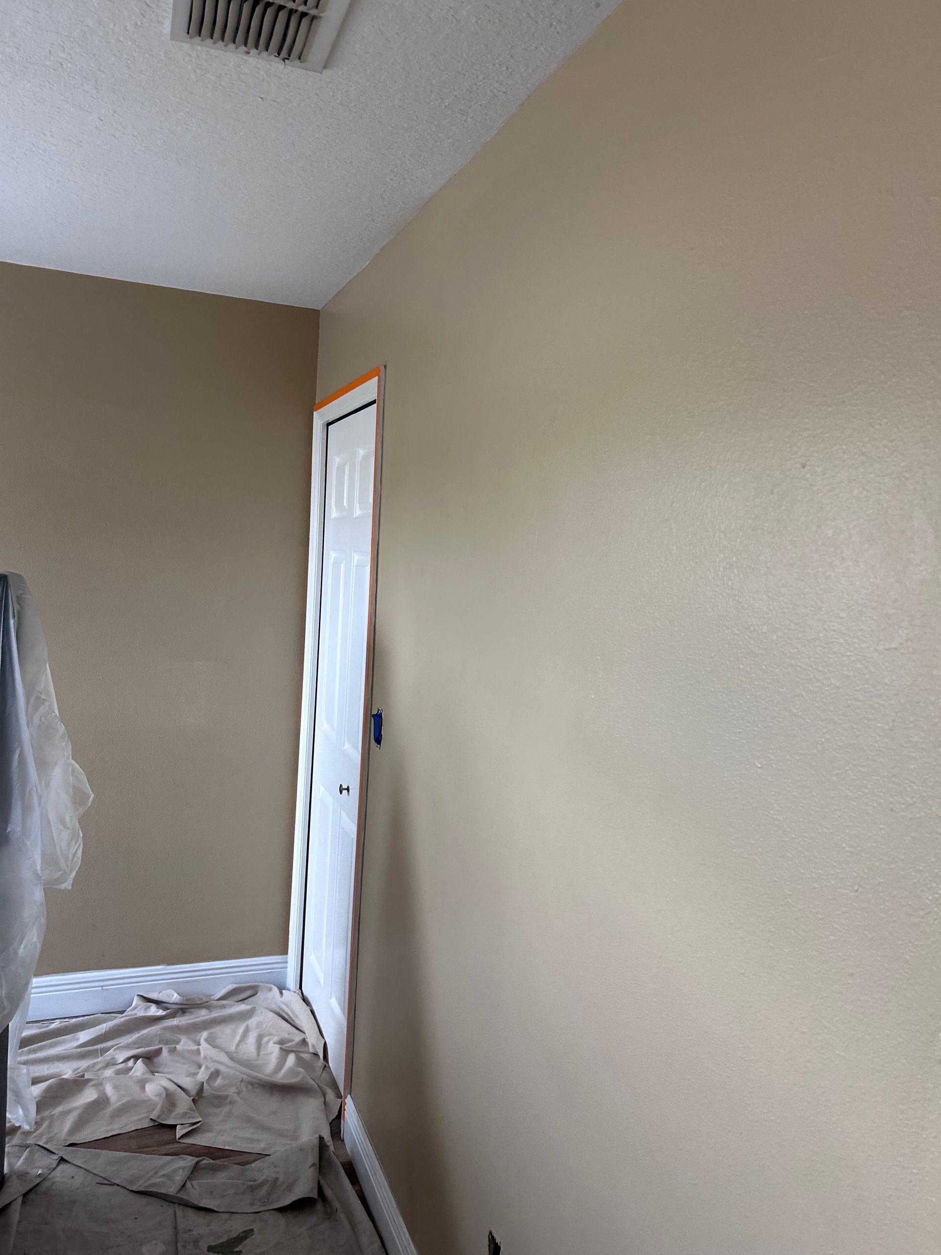 Room with painted tan walls, a white door, and protective covering on items.