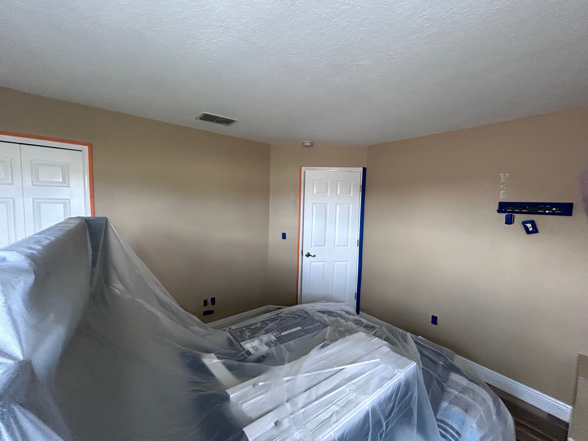 Room interior with beige walls, white doors, and furniture covered in plastic for protection.