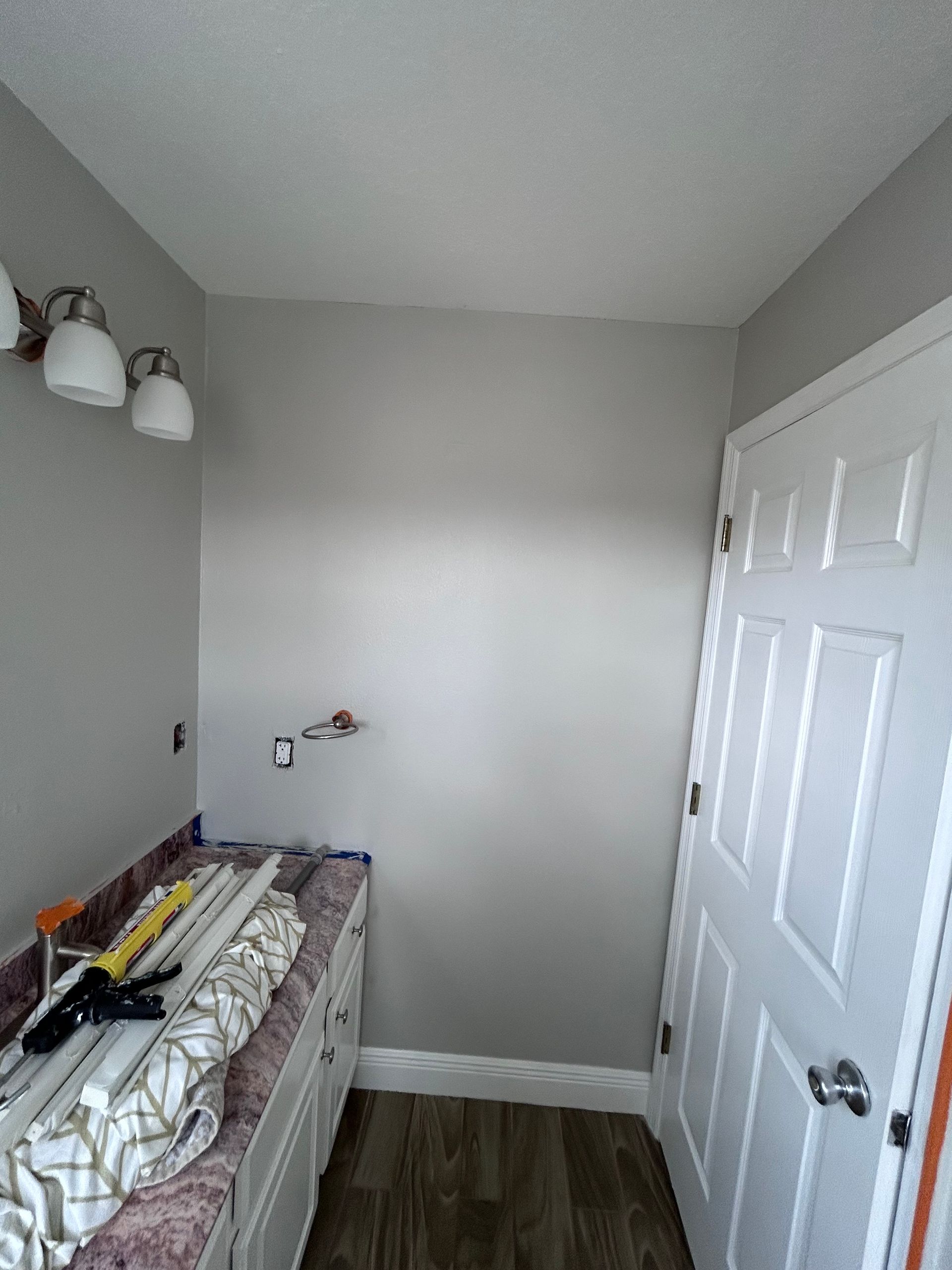 Bathroom interior with gray walls, white door and cabinets, and a vanity counter with fixtures and tools.
