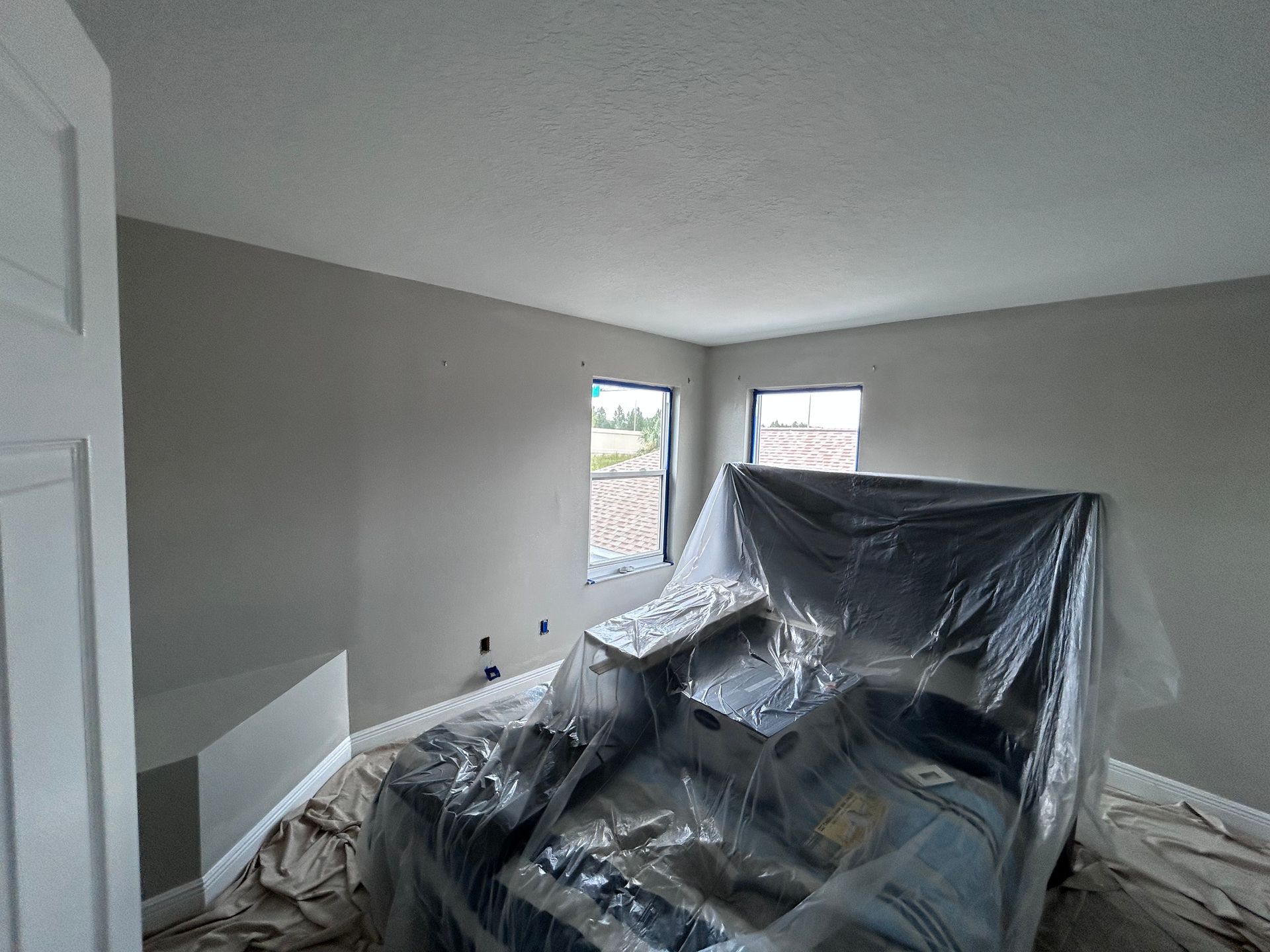 Interior of a room with gray walls, two windows, and a covered bed.