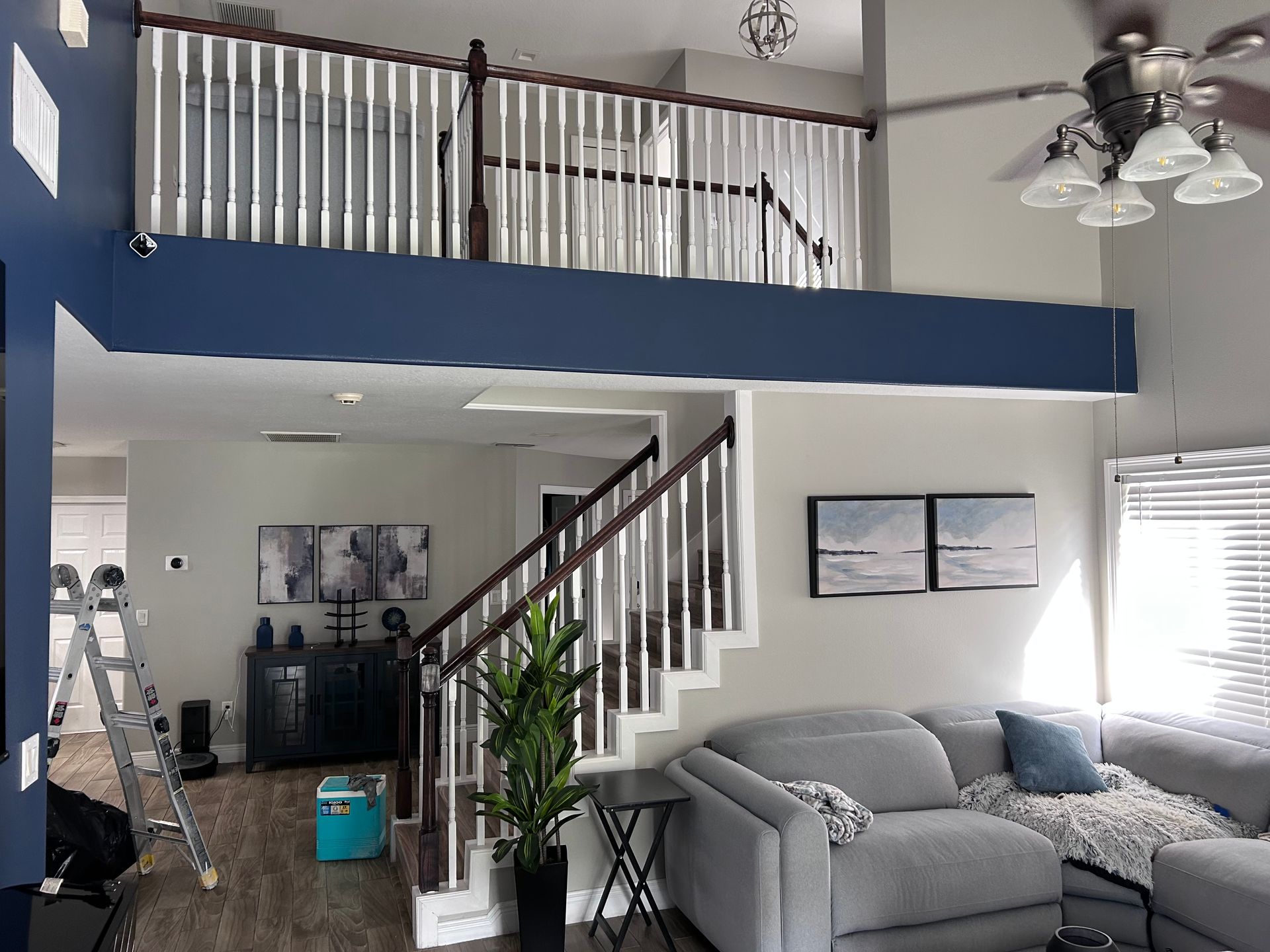 Interior of a two-story home with stairs leading to a loft. Blue accent wall and gray living room furniture.