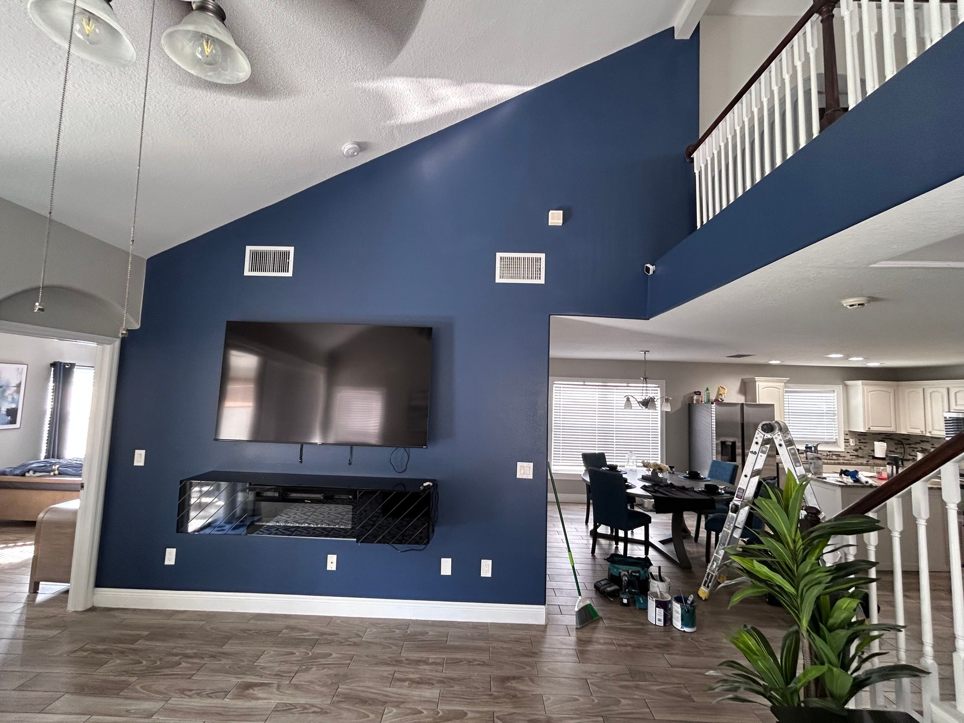Living room with high ceiling, blue accent wall, TV, and fireplace. Staircase on right, tile floors.