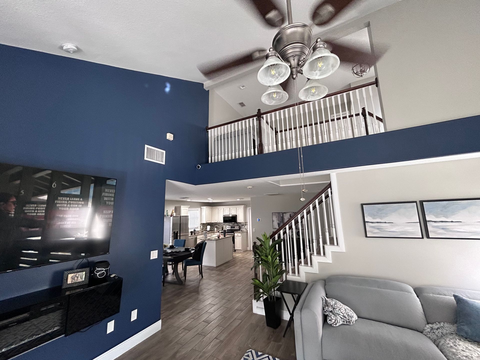 Living room with blue accent wall, gray couch, stairs leading to loft area.