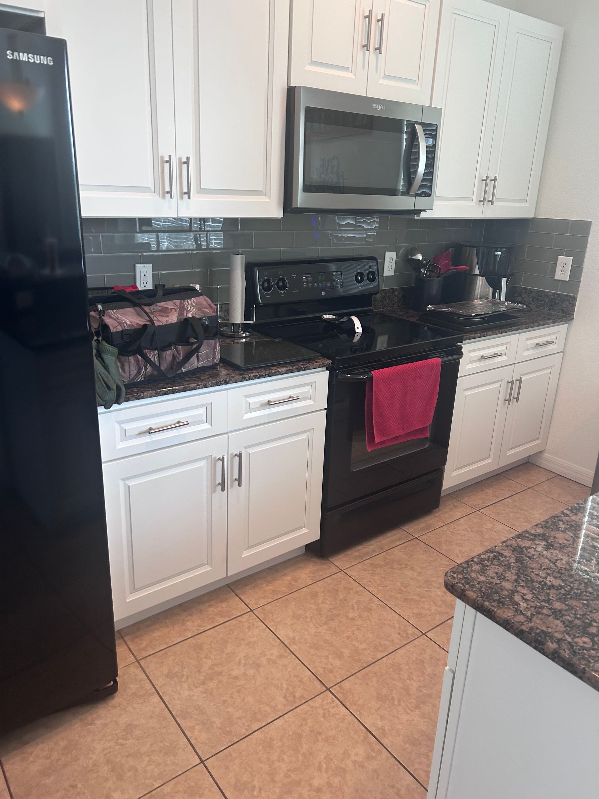 Kitchen with white cabinets, black appliances, dark countertops, and tile floor.