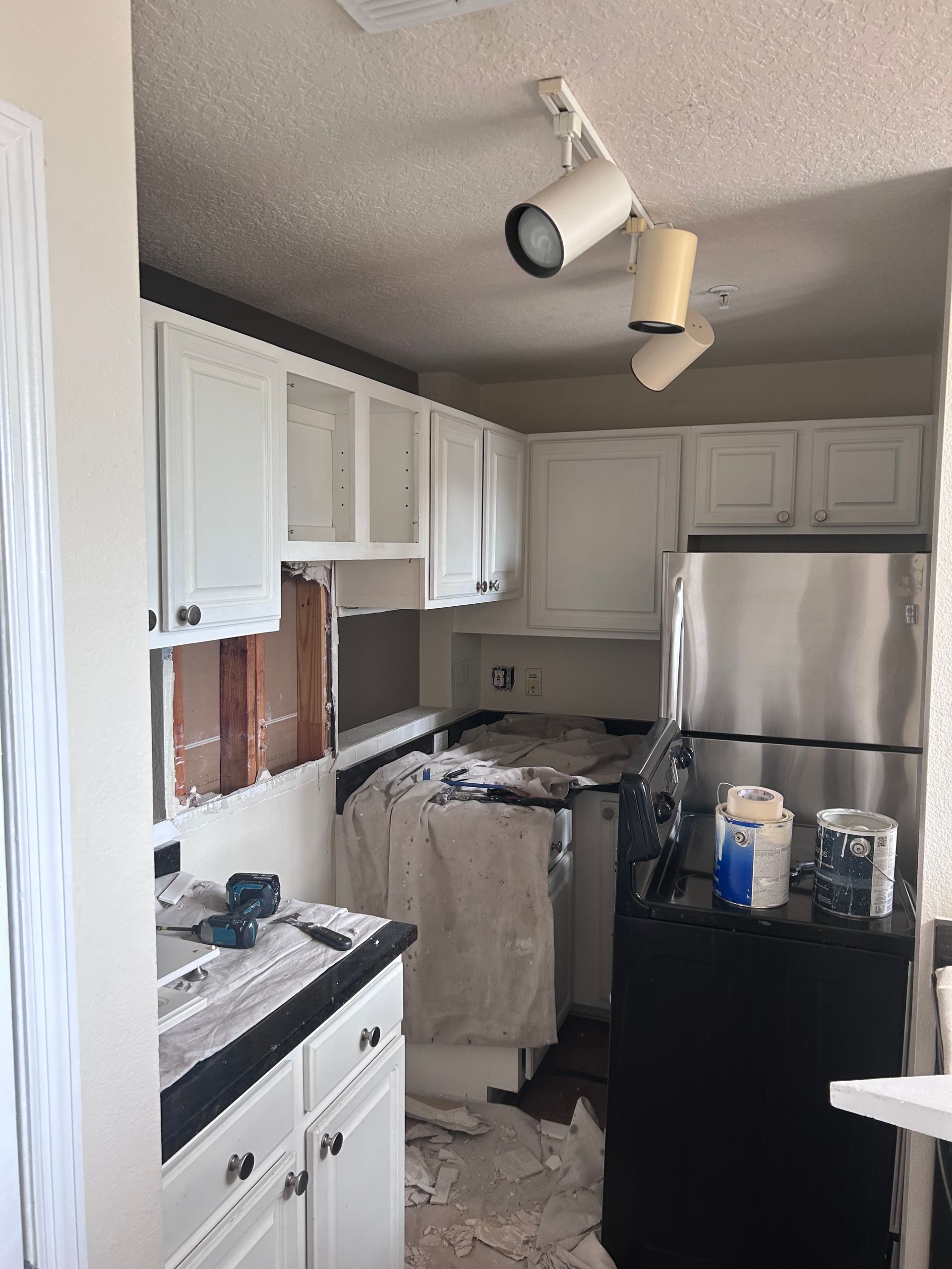 Kitchen under renovation with white cabinets, exposed wall, and appliances.