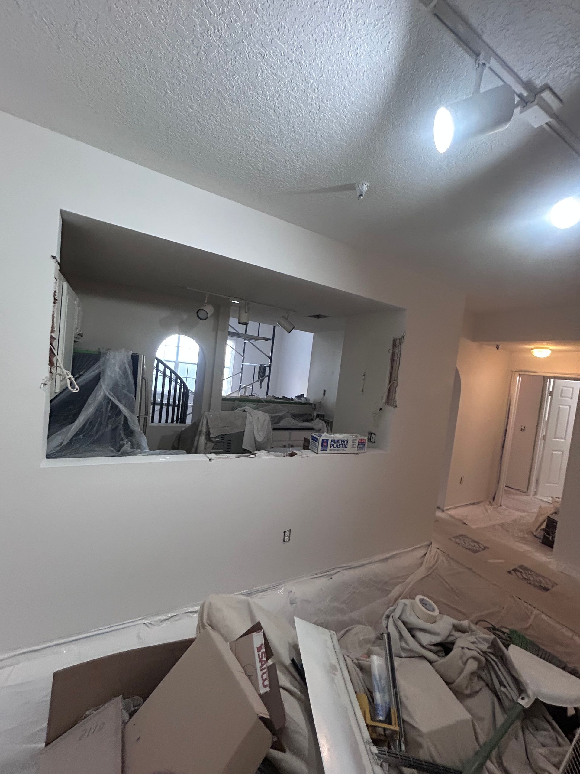 Interior renovation in progress, featuring a wall opening, debris, and partial views of other rooms.