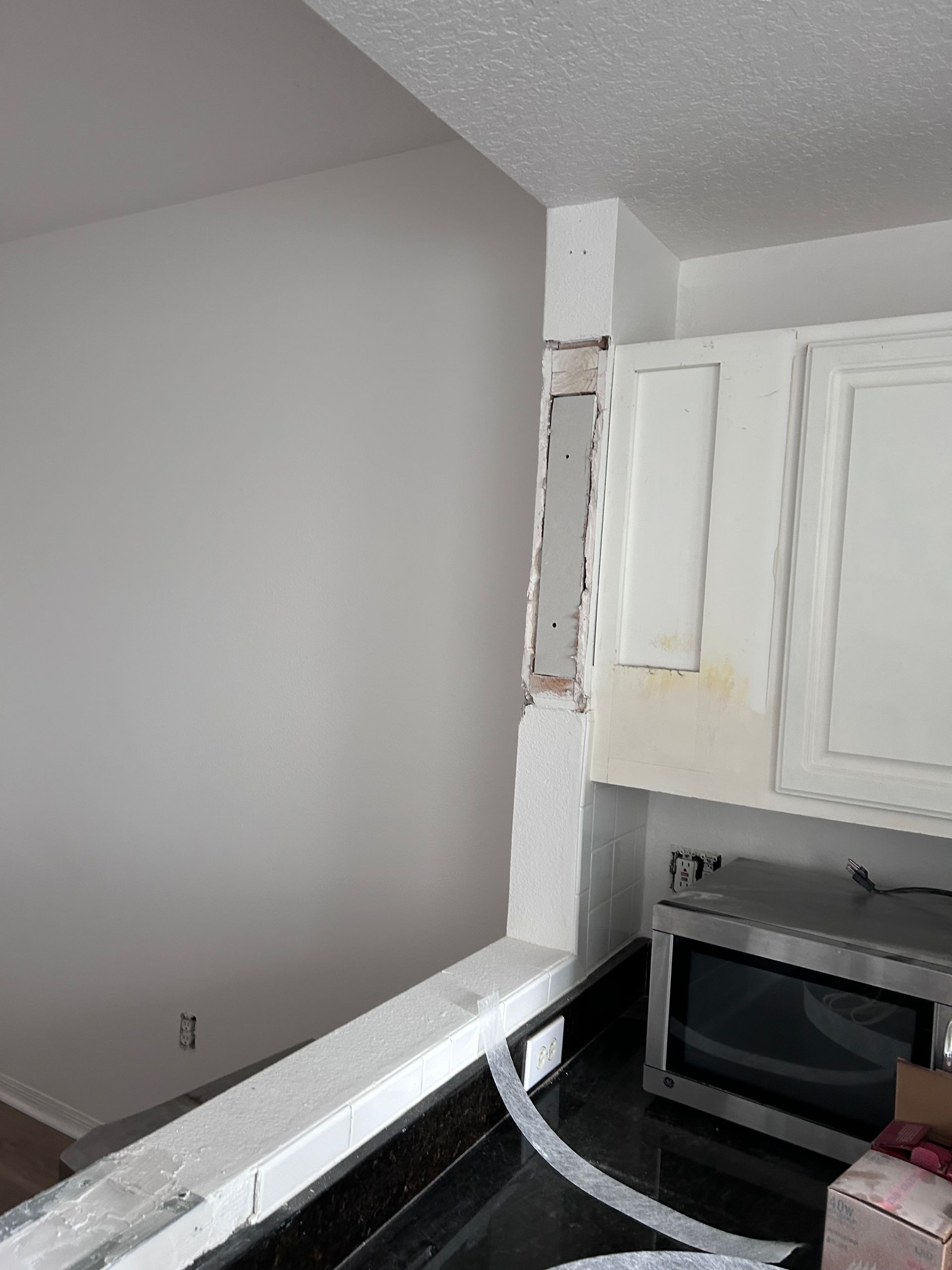 Kitchen remodel: Partially demolished wall with cabinets, countertop, and microwave.