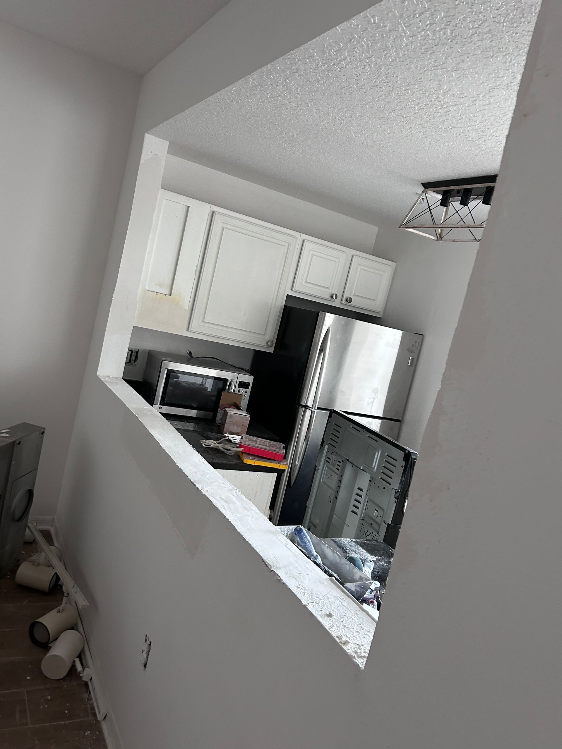 Opening in a white wall looking into a kitchen with white cabinets, stainless steel appliances, and a black countertop.