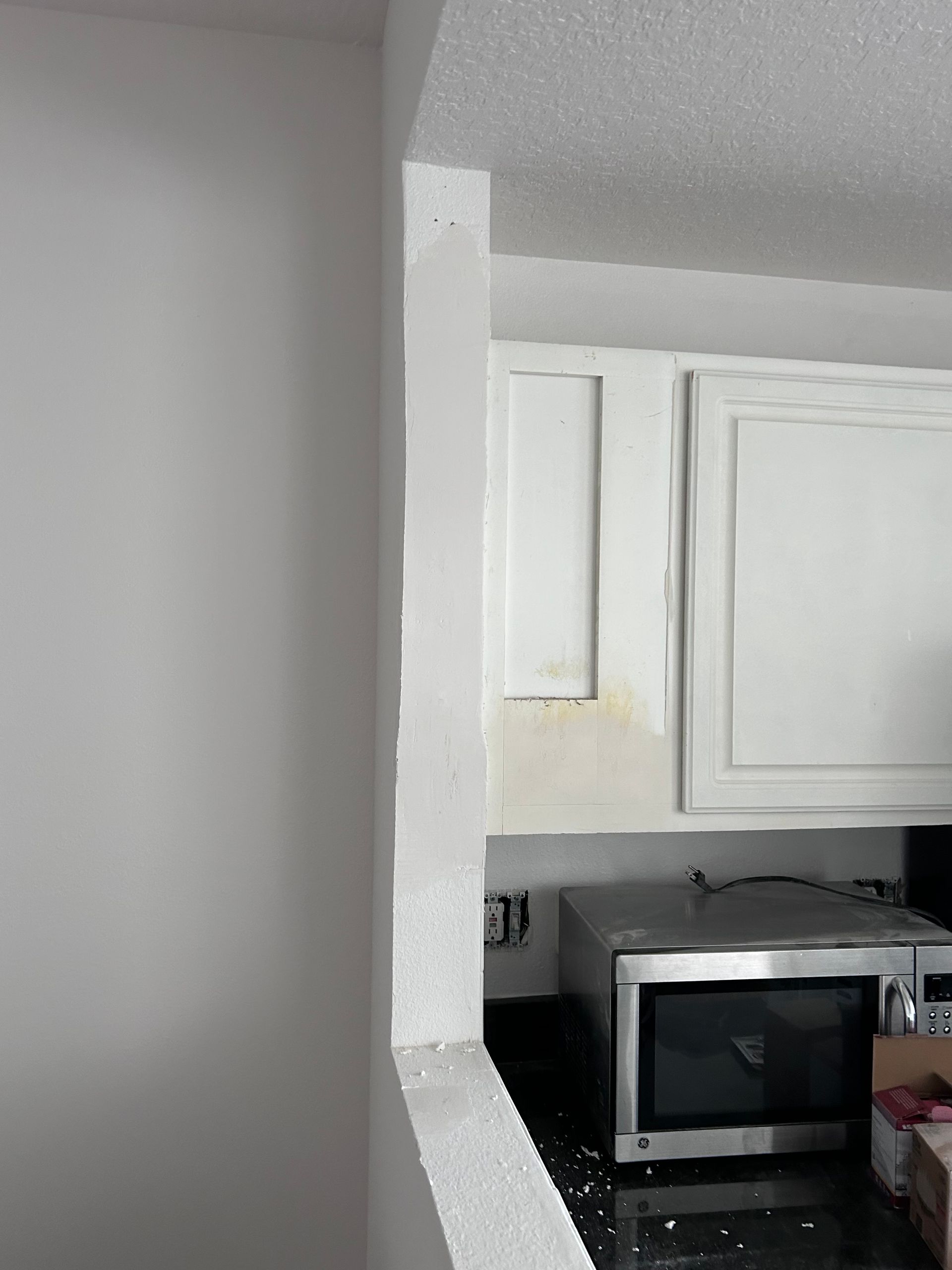 White kitchen cabinets and microwave viewed through a wall opening.