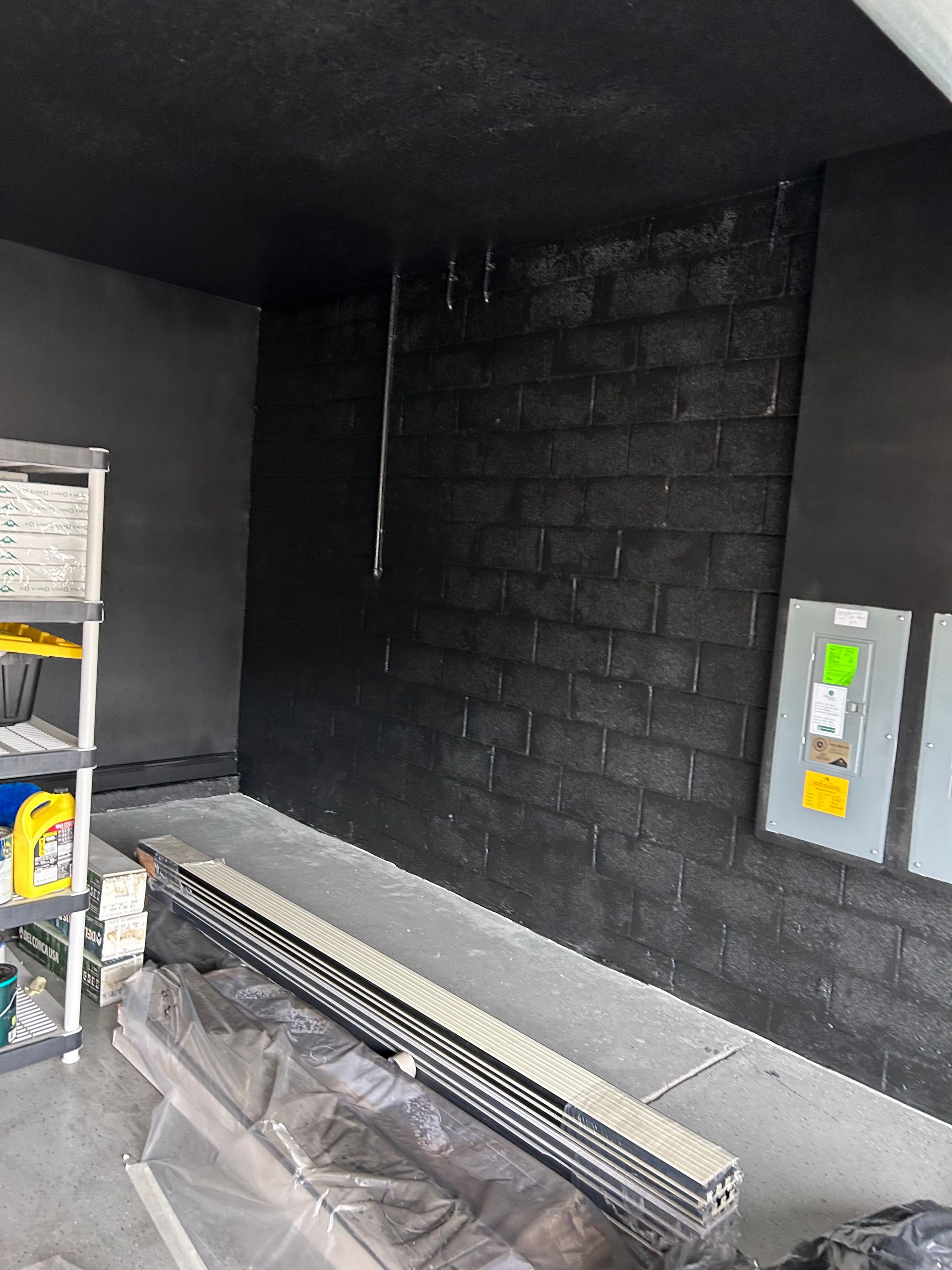Black painted brick wall in a garage, with shelves and equipment. Gray floor.