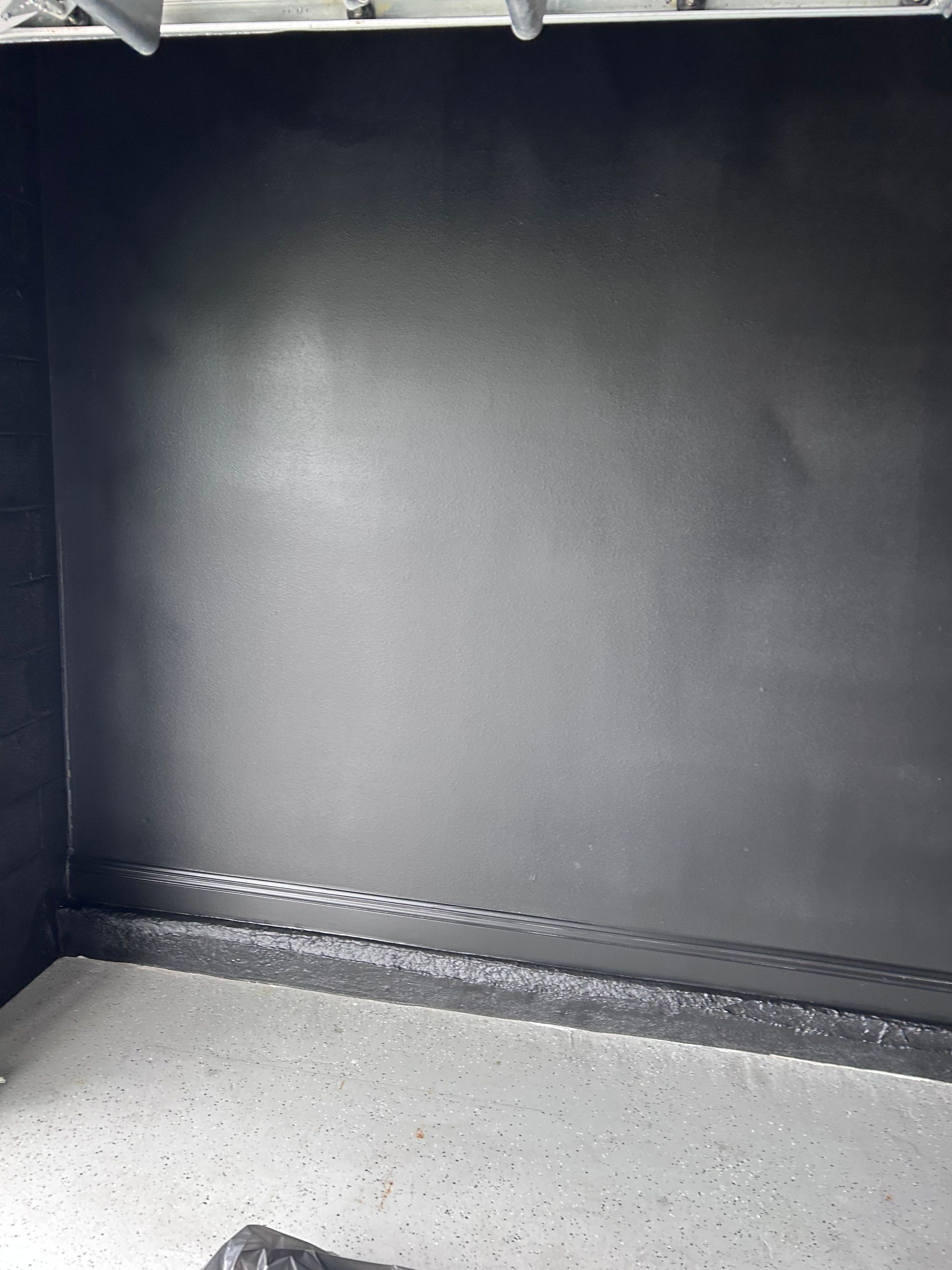 Dark interior of a cabinet with black walls and a speckled gray floor.