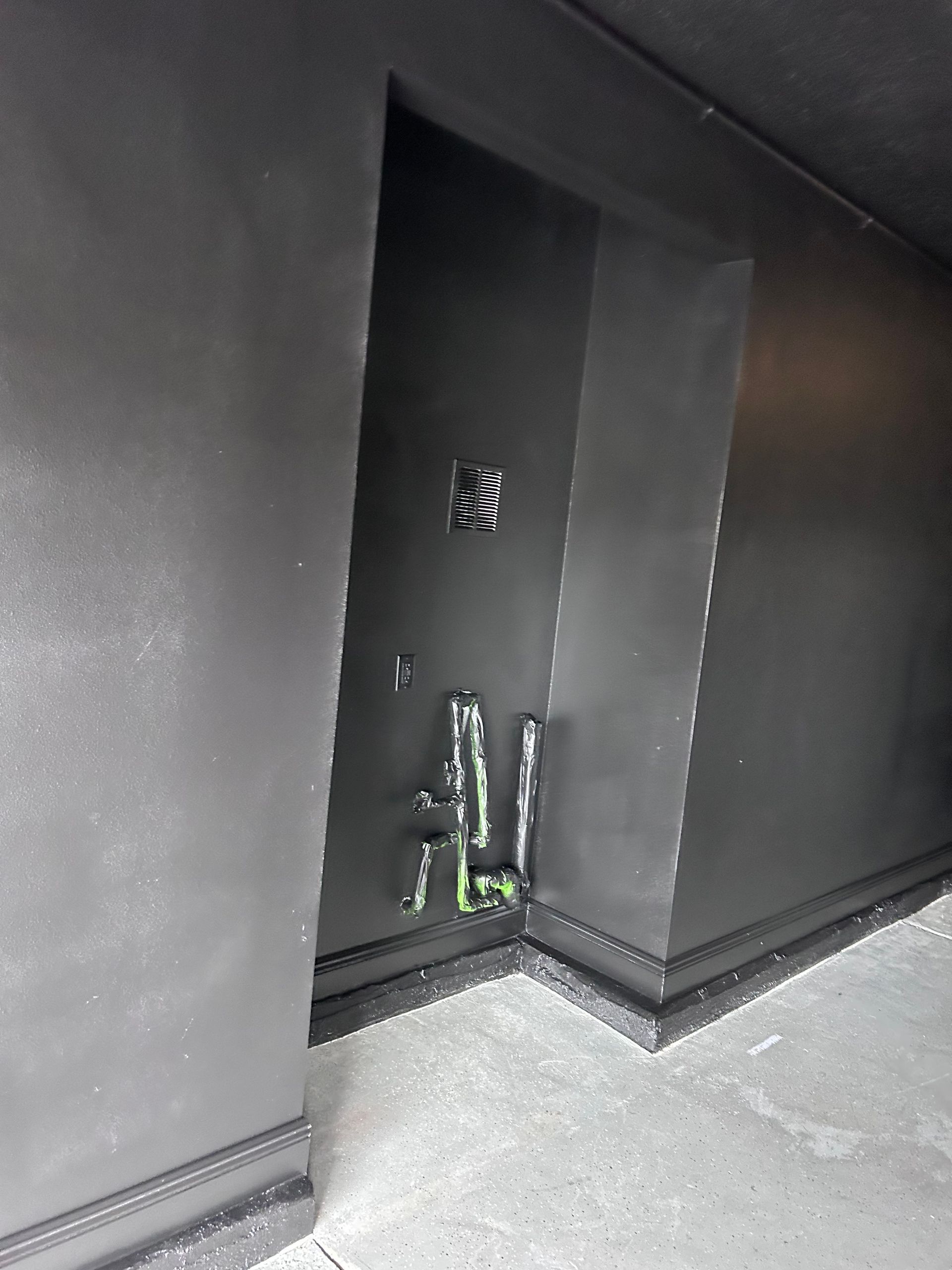 Black painted room corner with unfinished electrical work protruding from the wall.