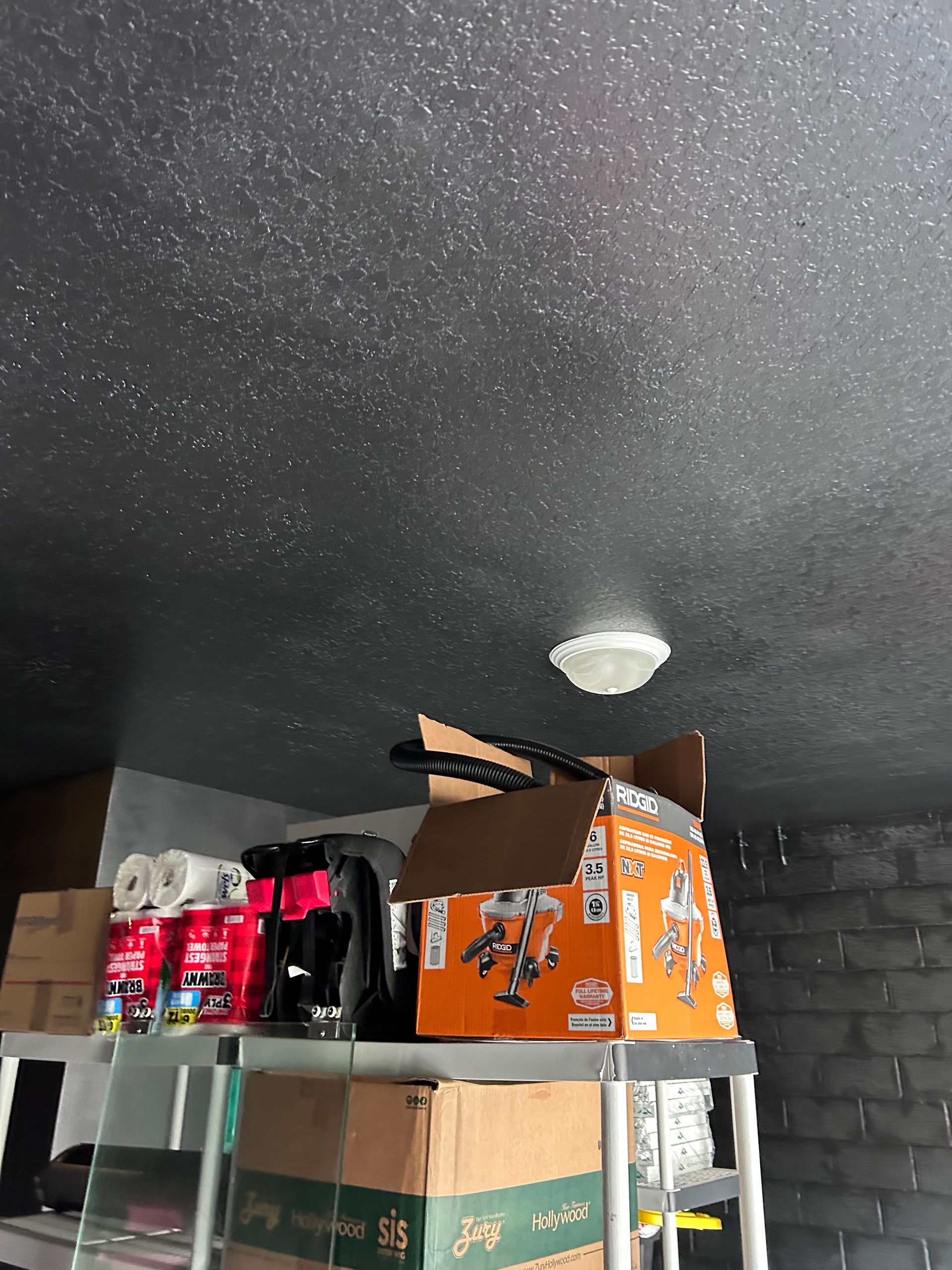 Garage interior; a shelf with boxes, tools, and paper towels under a speckled gray ceiling.
